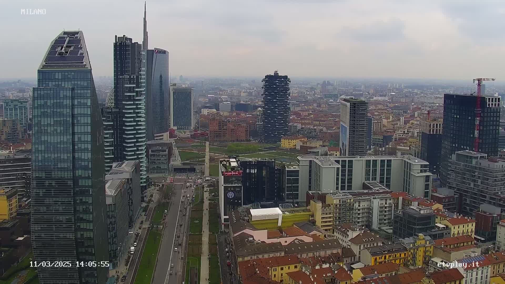A sprawling cityscape of Milan on an overcast day, showcasing a mix of modern skyscrapers and traditional low-rise buildings.