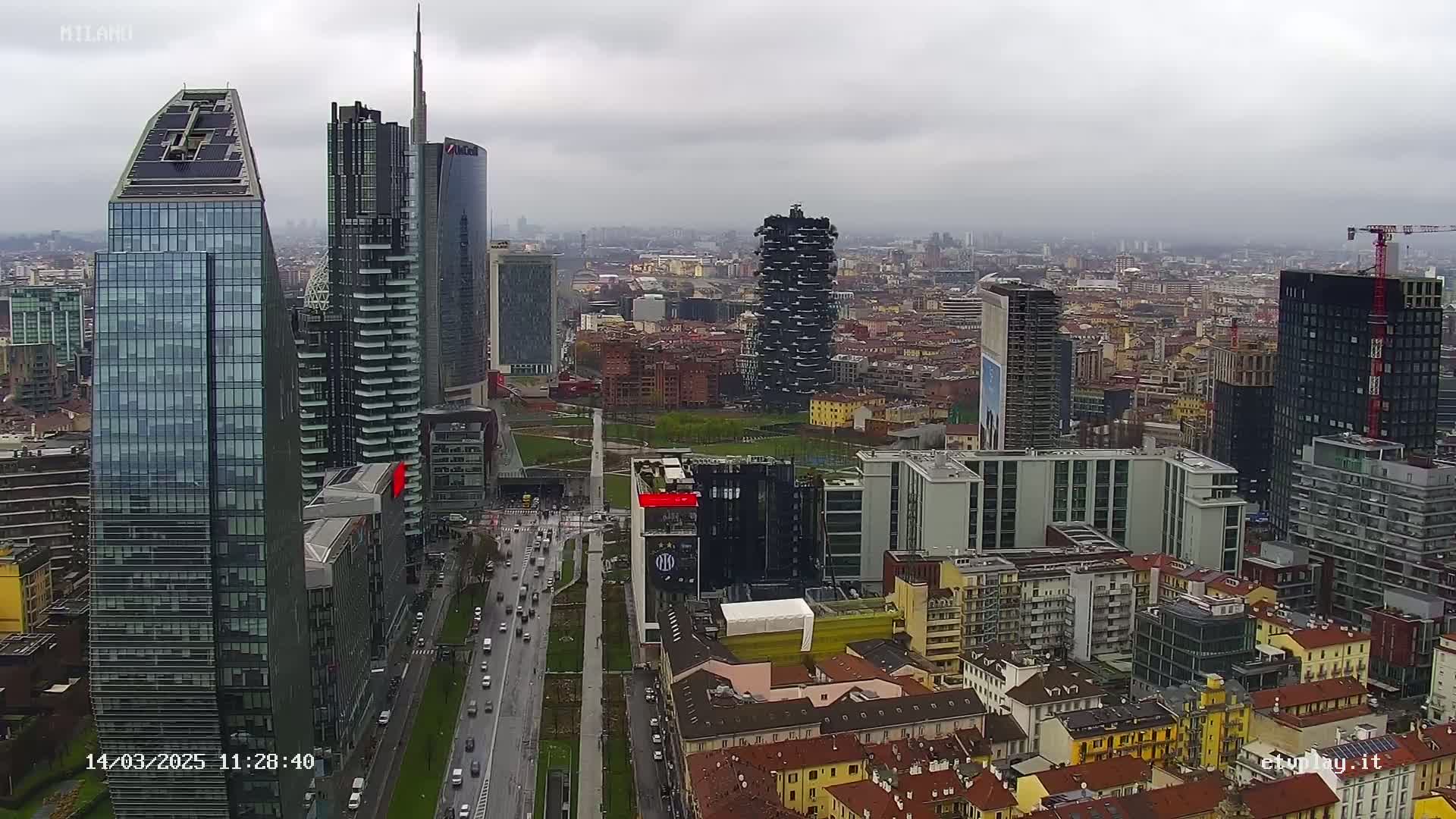 A high-angle view of a city skyline on an overcast day, showing numerous skyscrapers and surrounding buildings, with a road visible below.
