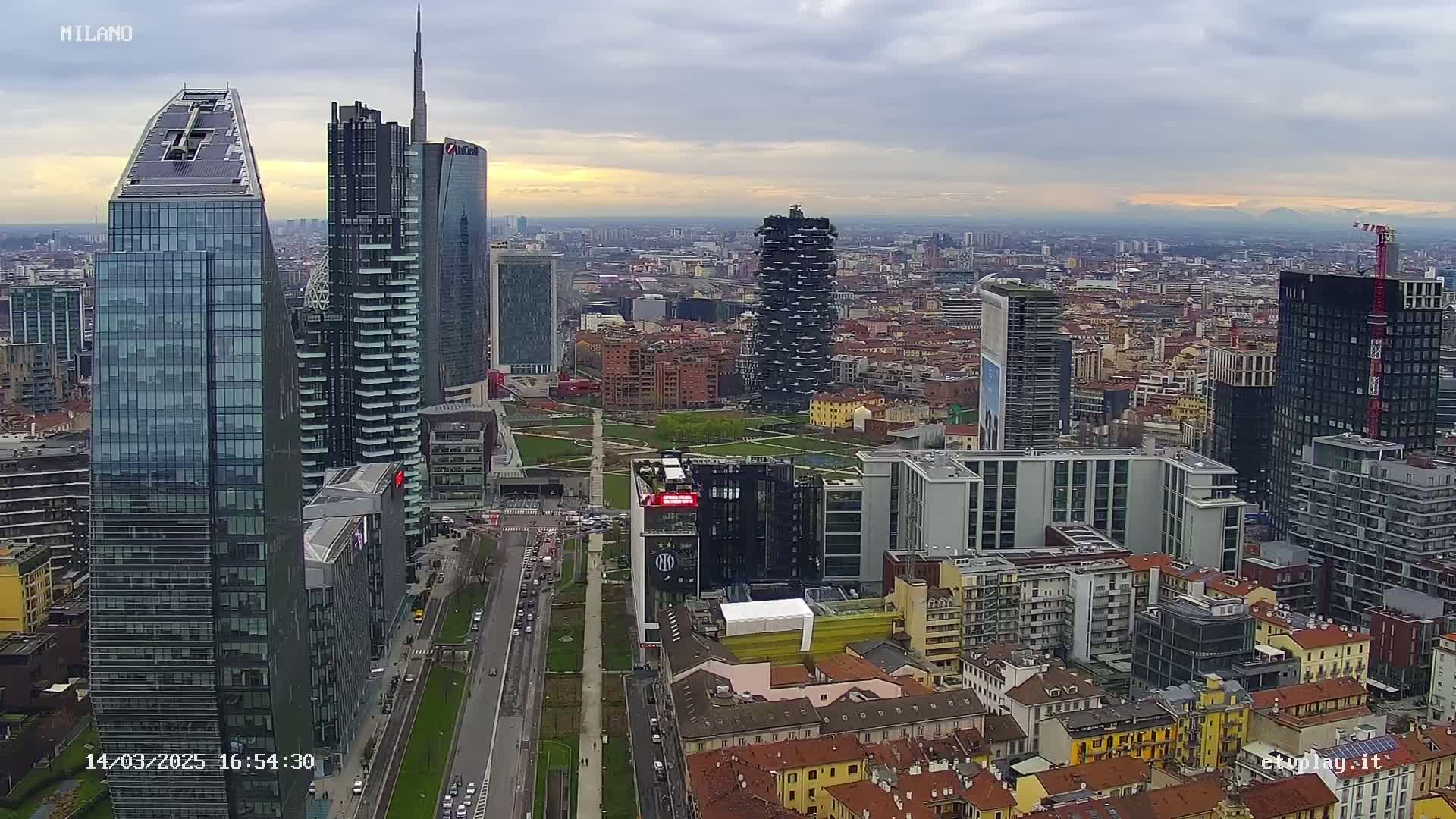 An aerial view of a city skyline shows numerous skyscrapers under a cloudy sky.