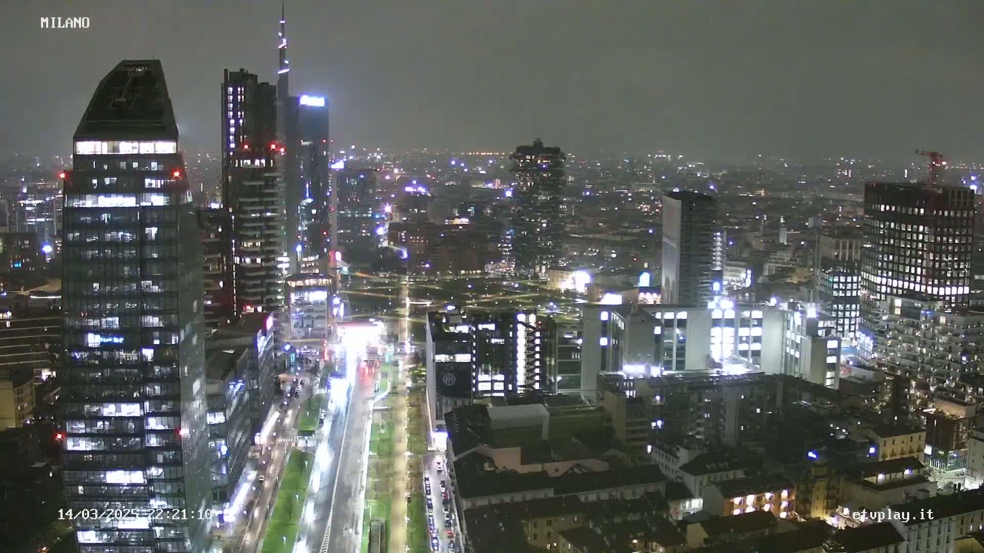 A nighttime aerial view of a city with numerous illuminated skyscrapers and streets, under overcast conditions.