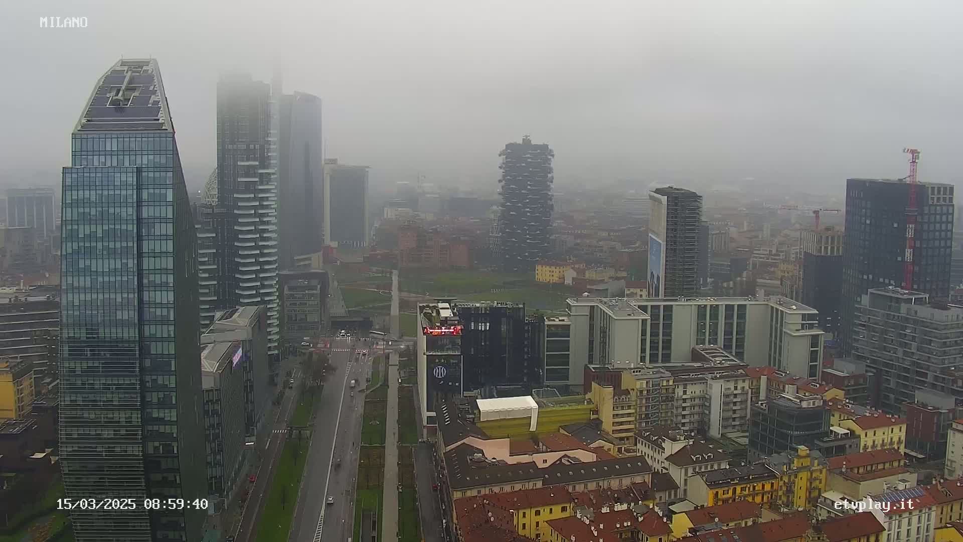A foggy cityscape view of numerous skyscrapers and buildings, with a wide street below.