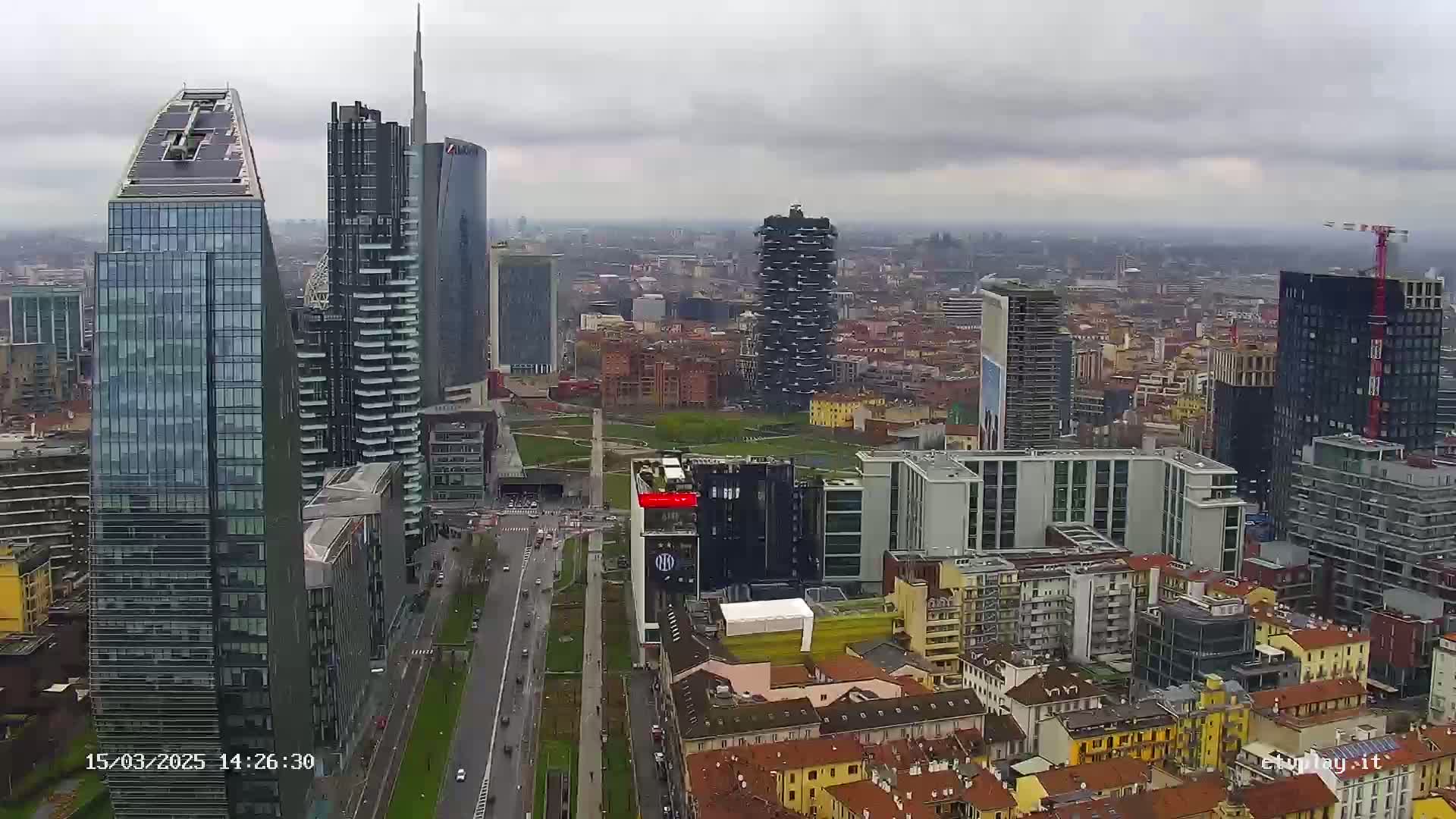 A high-angle, long shot of a city with numerous skyscrapers under an overcast sky.