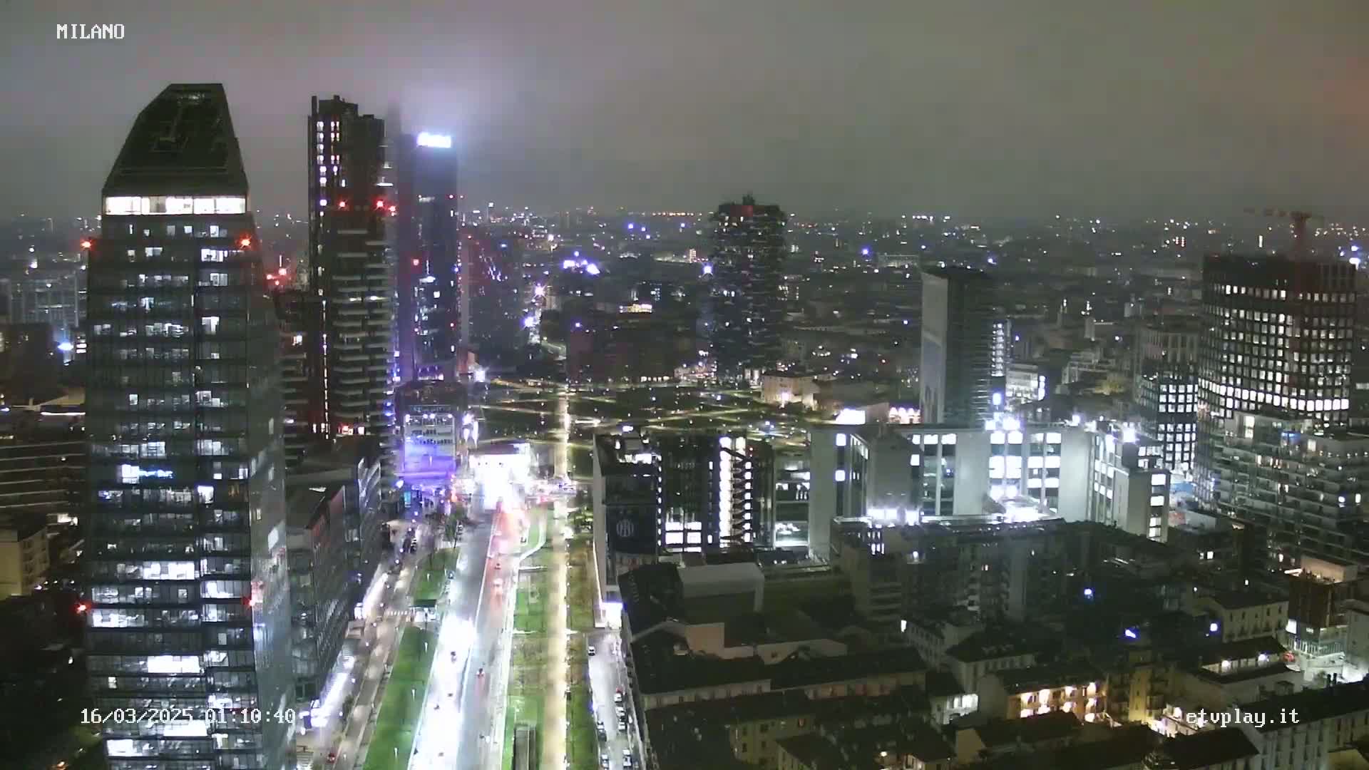 A nighttime, hazy view of a city with many tall buildings and brightly lit roads.