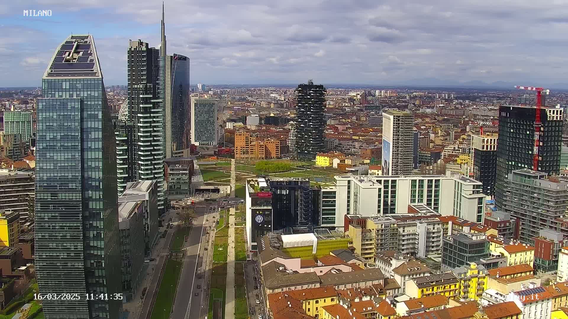 An aerial view of a city with many modern skyscrapers under a partly cloudy sky.