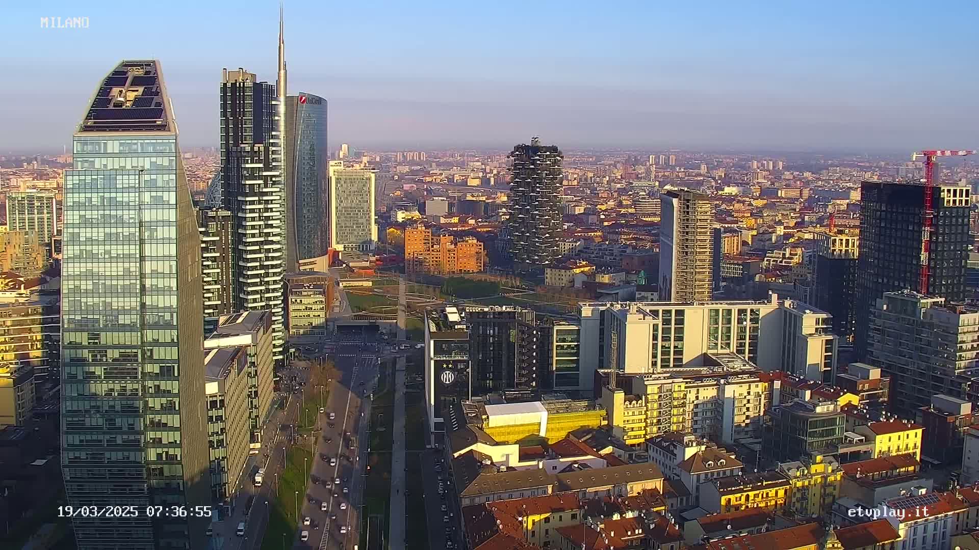 An aerial view of a dense cityscape at sunset, with numerous skyscrapers and other buildings, under a clear sky.