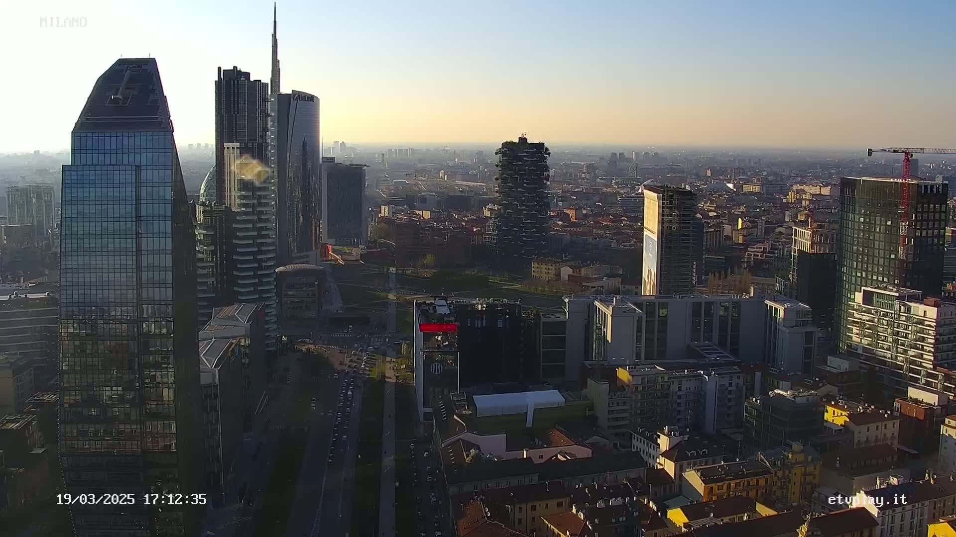 An aerial view of a city skyline at sunset, showing numerous skyscrapers and surrounding buildings under clear skies.