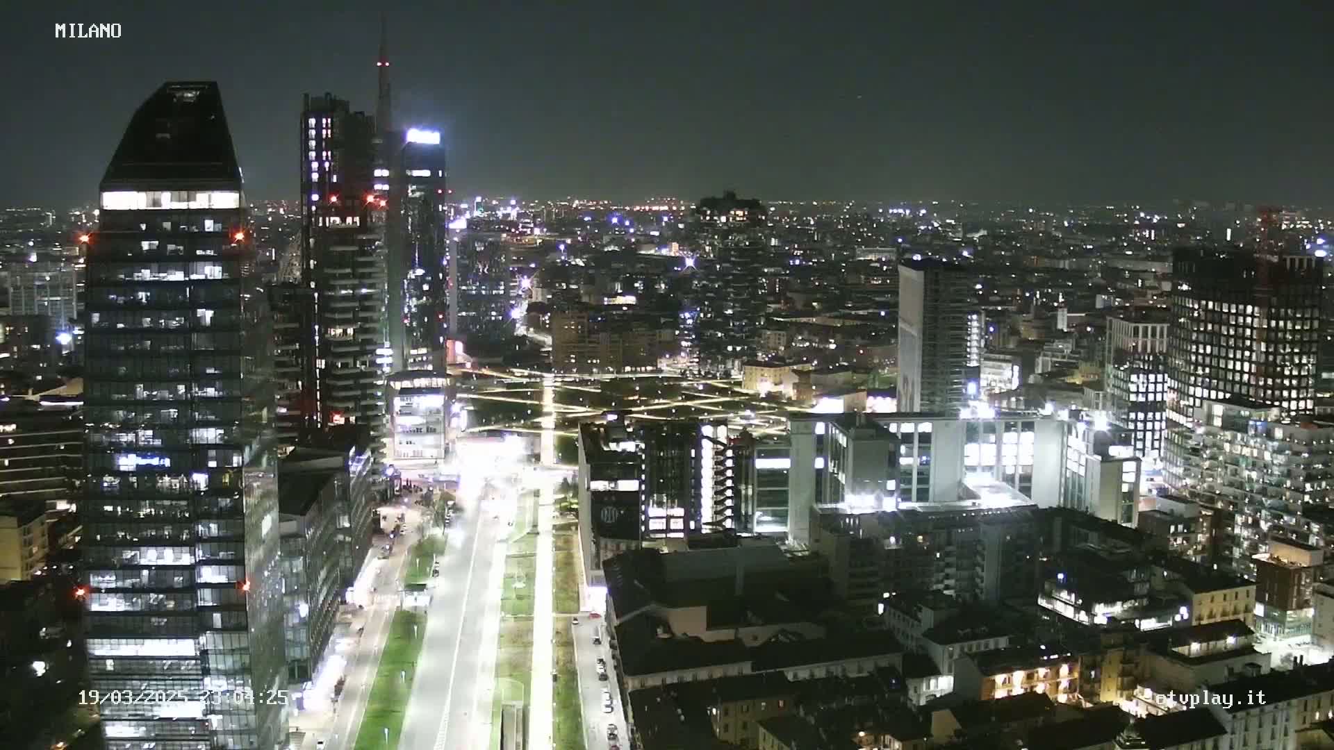 A nighttime aerial view of a city, showing brightly lit skyscrapers and streets, under a clear, dark sky.