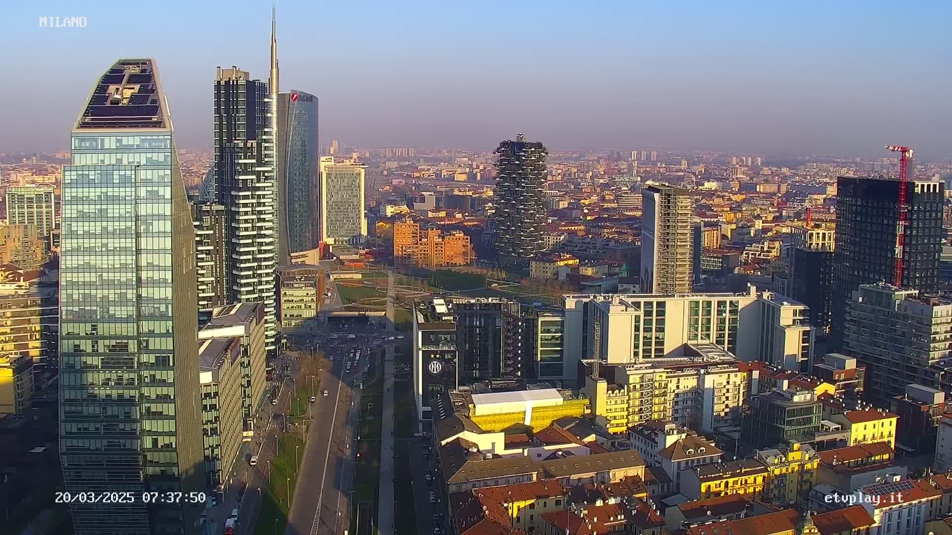 An aerial view of a city skyline with many modern skyscrapers under a clear, bright sky.
