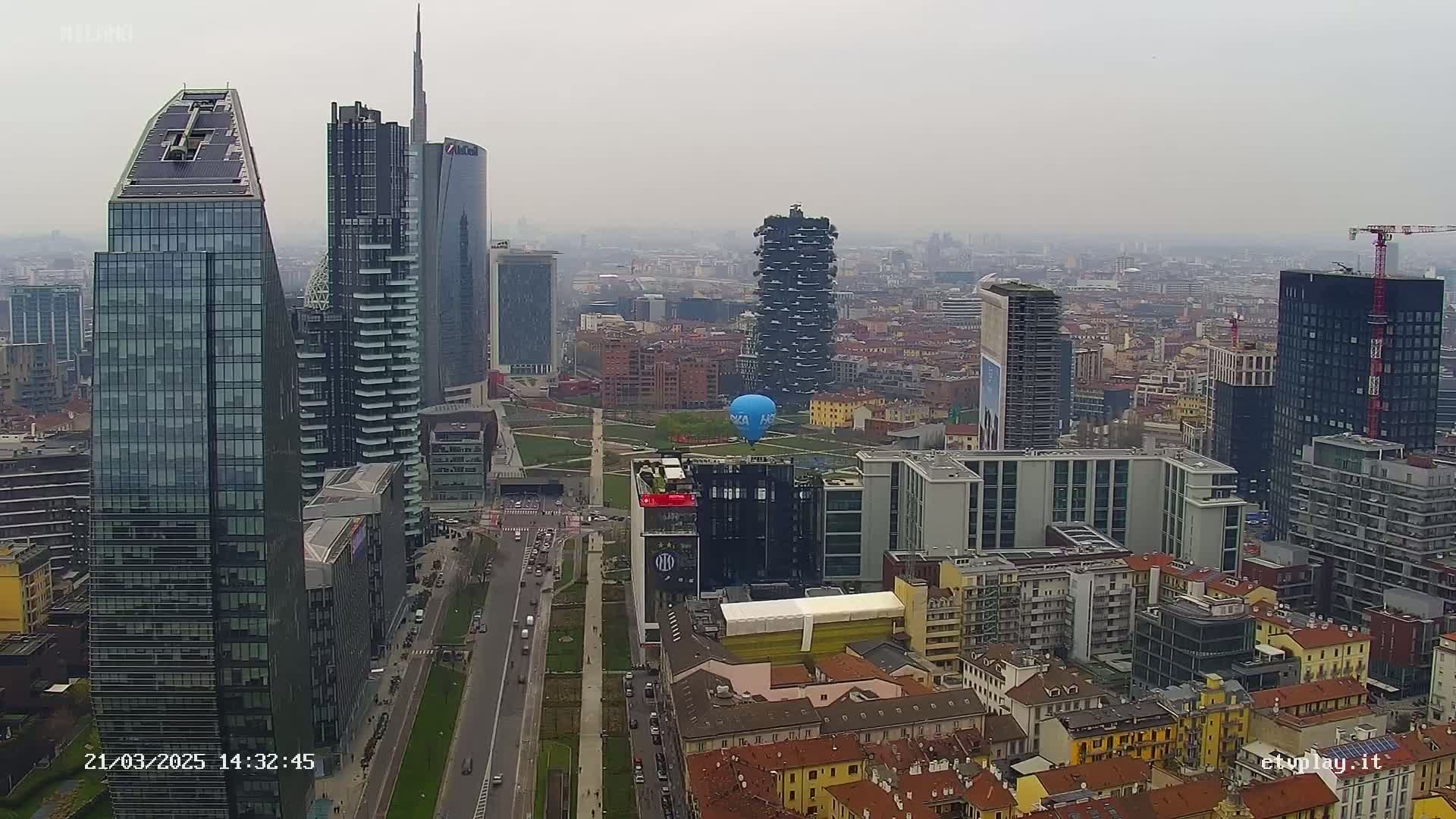 A hazy cityscape with numerous skyscrapers and a lone hot air balloon hovering over a park-like area.