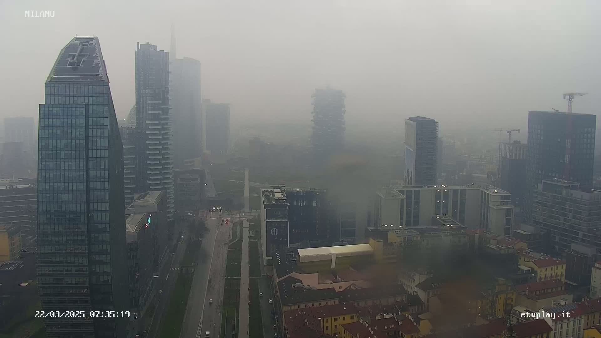 A foggy cityscape shows numerous skyscrapers and shorter buildings, with a wide street running through the center.
