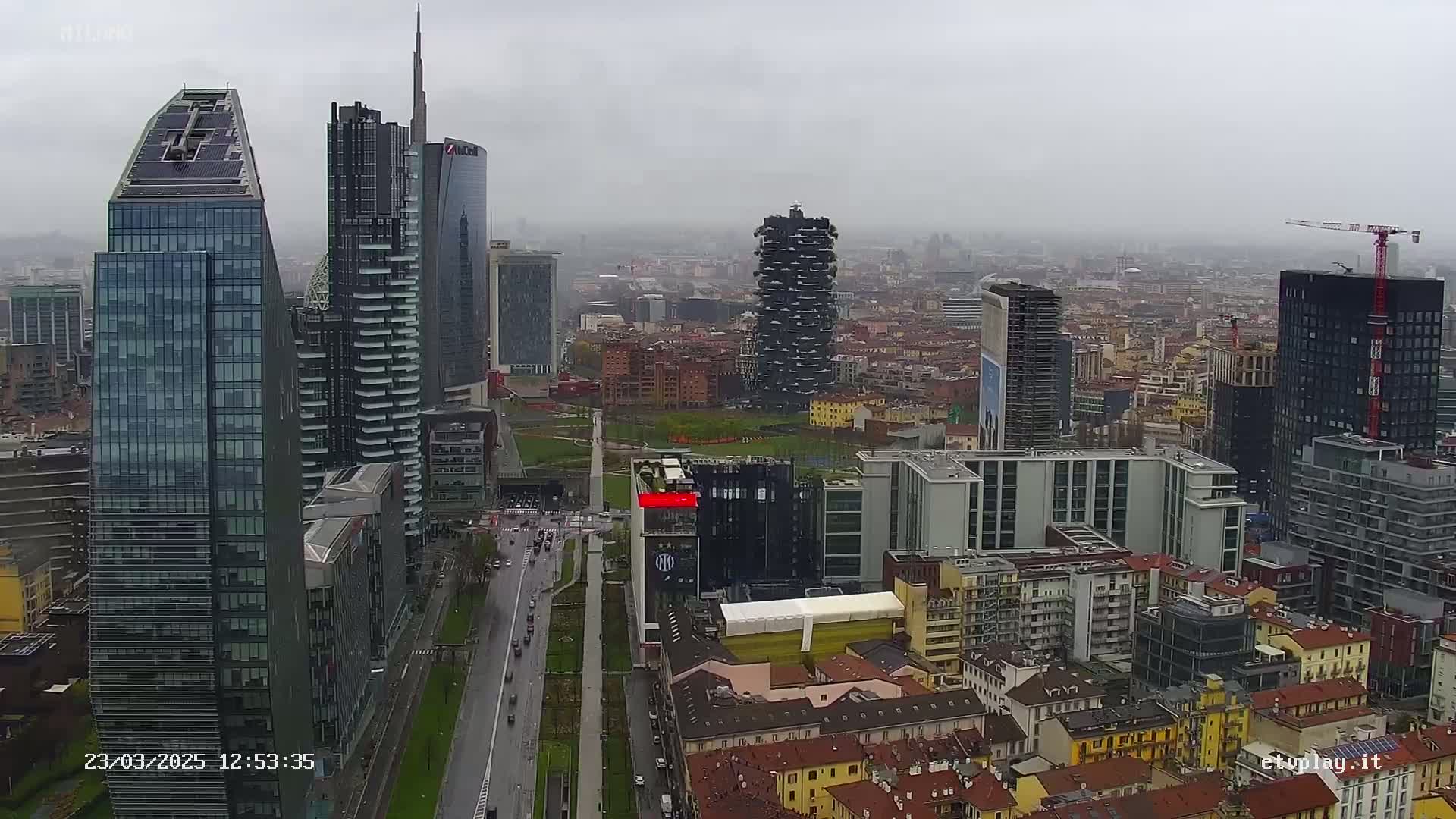 A city skyline of many skyscrapers and other buildings on an overcast day with light rain or drizzle.