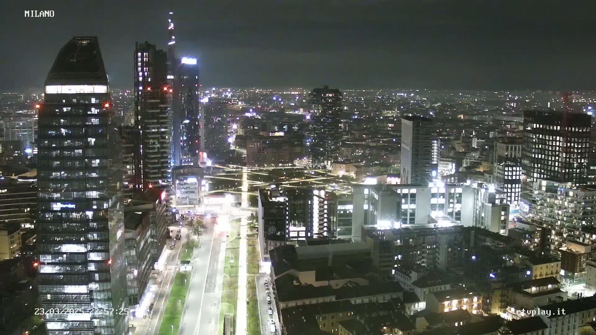 A nighttime, high-angle view of a city skyline illuminated by lights, showing numerous buildings and streets.
