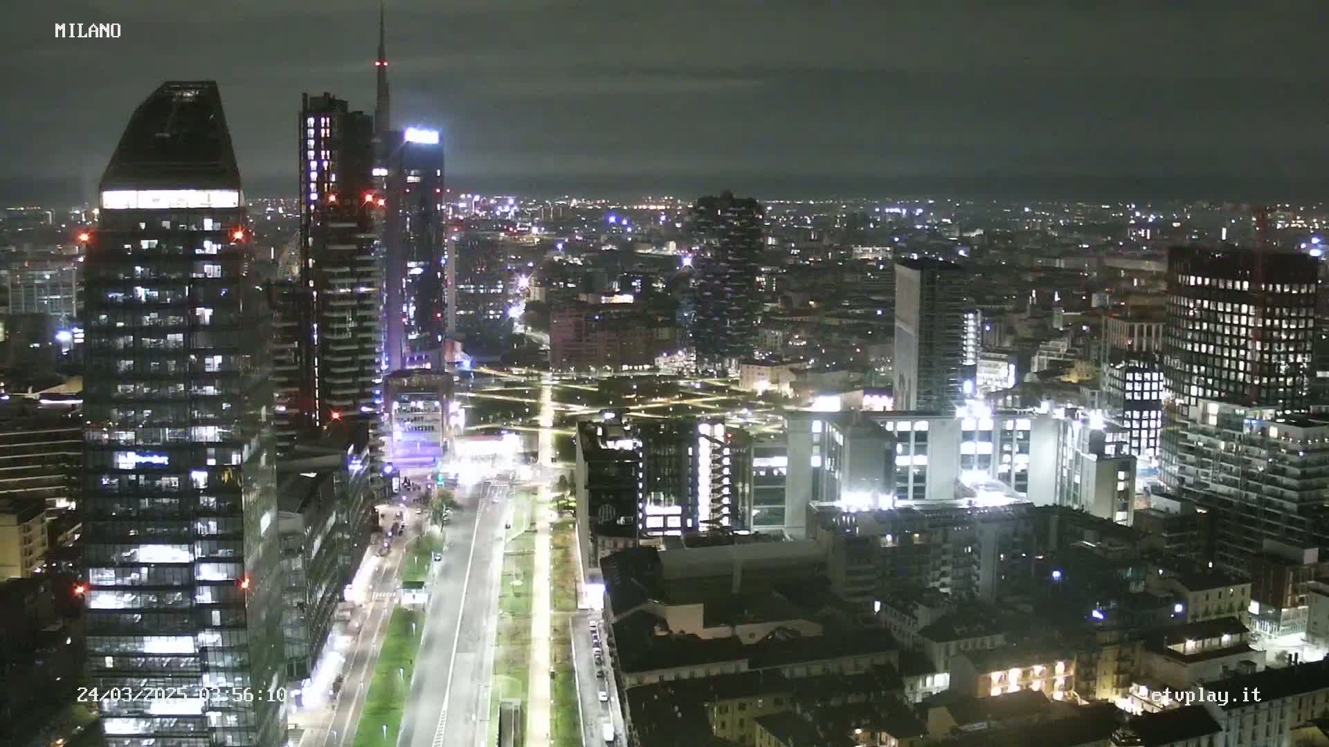 A nighttime aerial view of a city skyline with many illuminated skyscrapers and streets under a mostly clear sky.