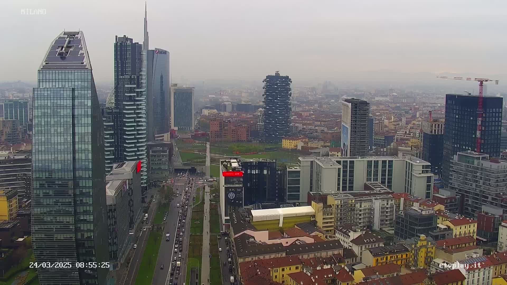 A hazy, overcast day reveals a dense cityscape of modern and older buildings, with a highway visible below.