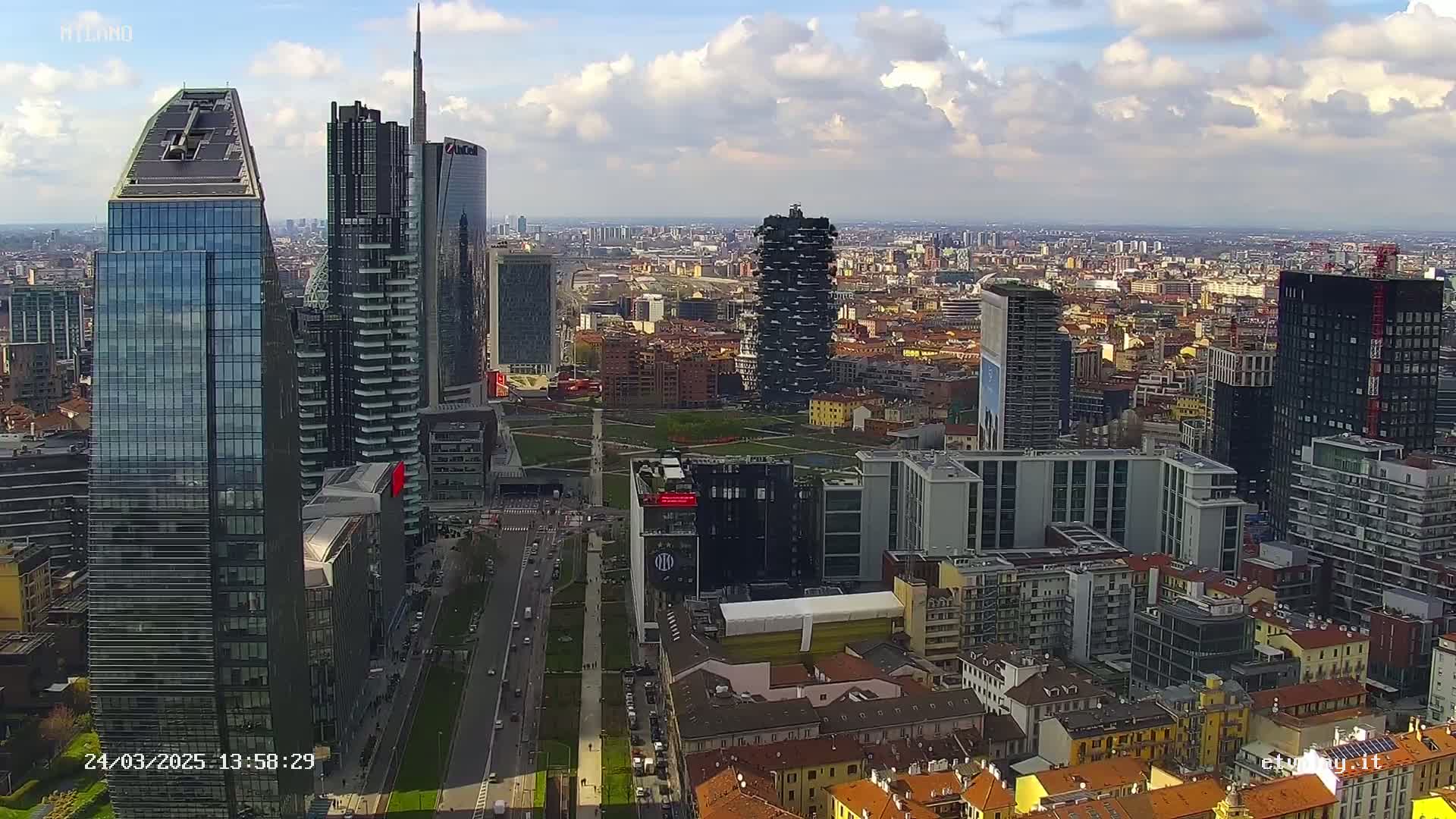 An aerial view of a city with numerous skyscrapers under a partly cloudy sky.