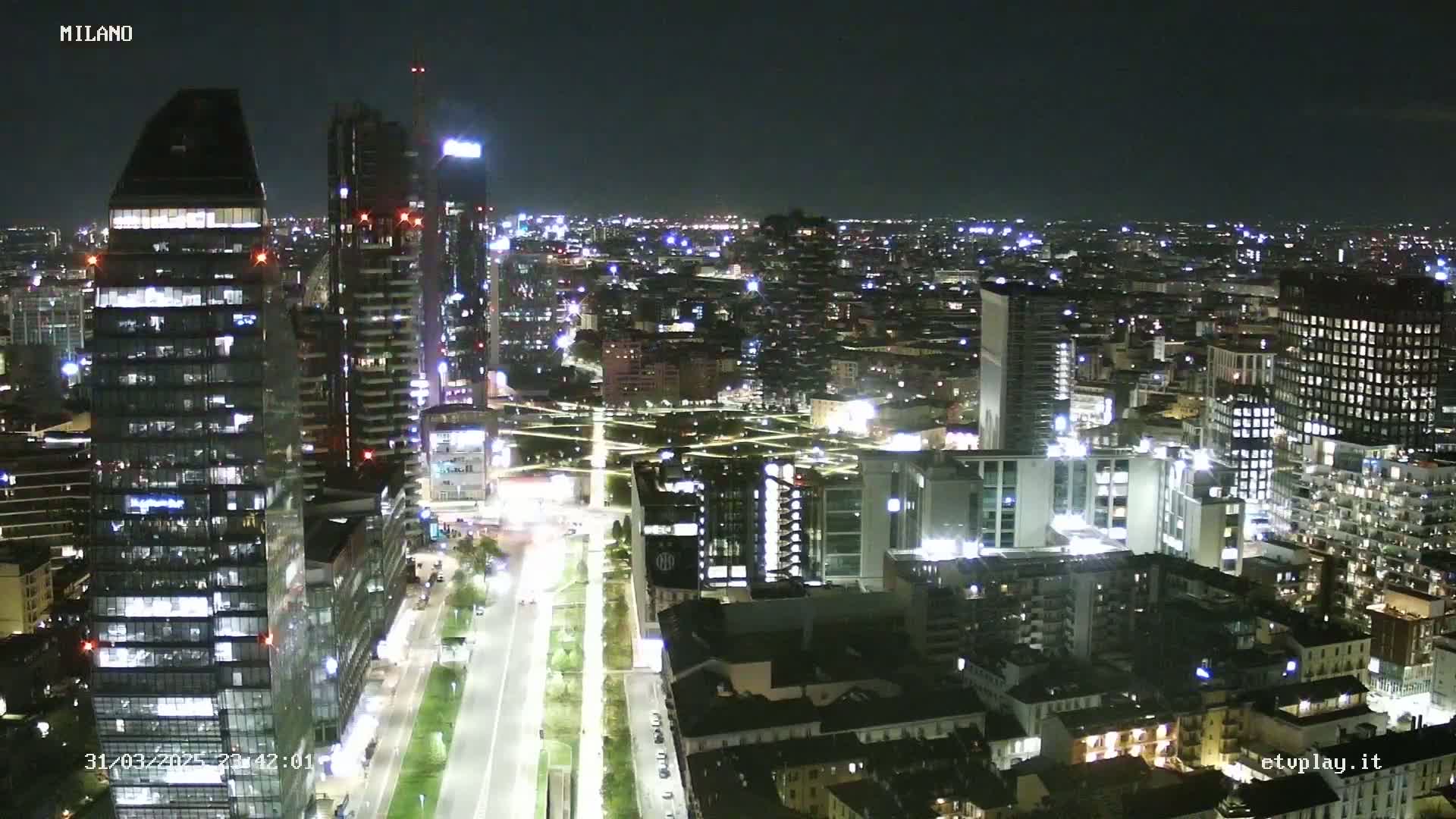 A nighttime aerial view of a city with numerous illuminated skyscrapers and buildings, showing a clear sky.