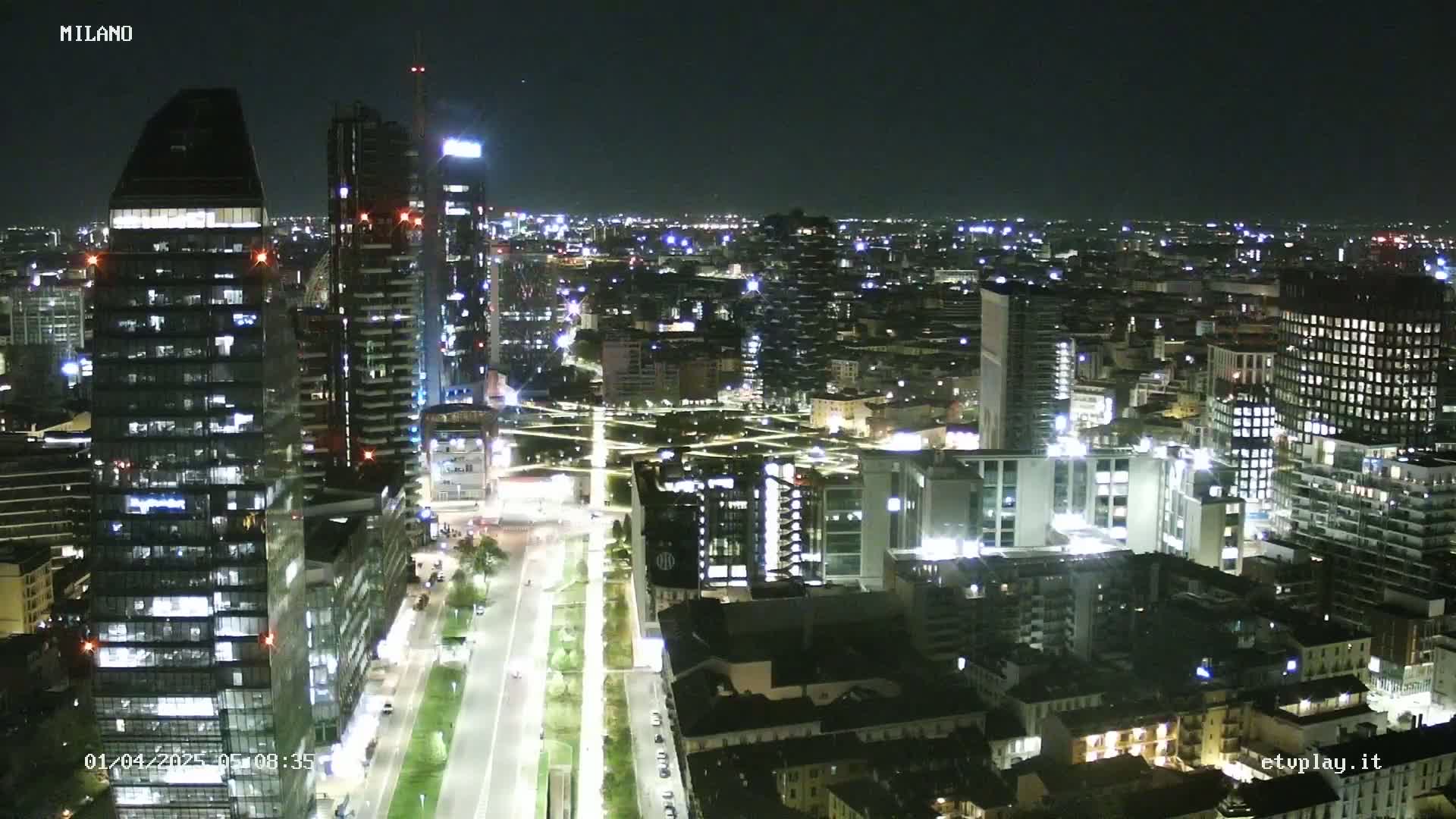 A nighttime, high-angle view of a city with numerous illuminated buildings and streets, showing a wide expanse of urban development.