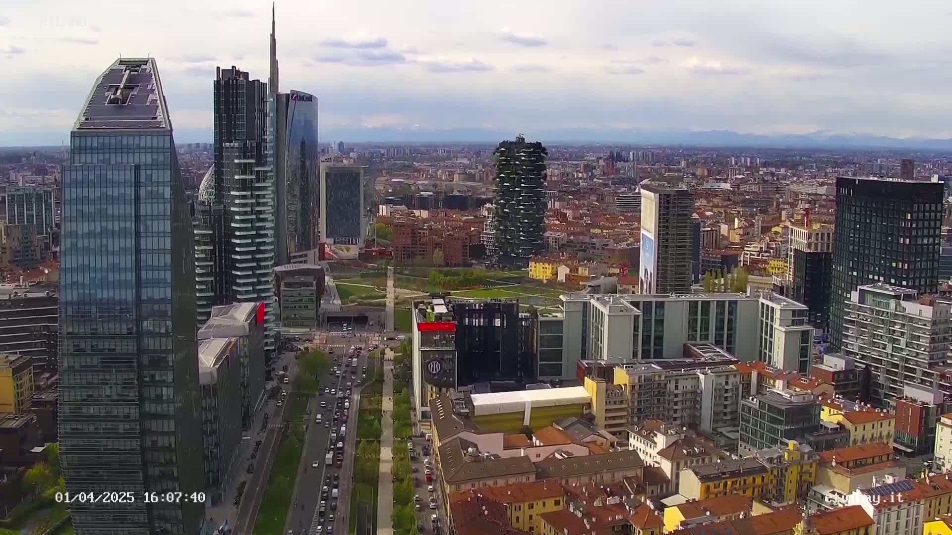 An aerial view of a city skyline with many modern skyscrapers under partly cloudy skies.