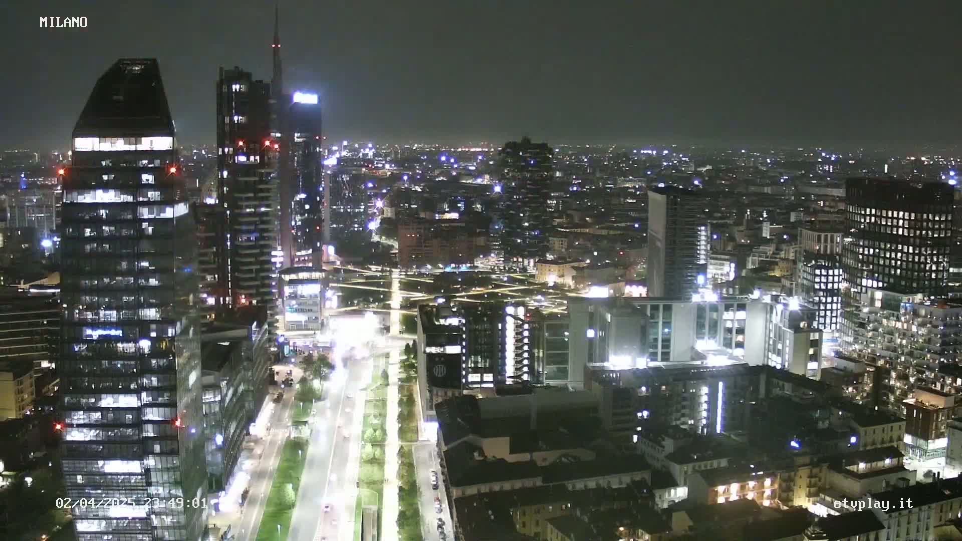 A nighttime aerial view of a city with numerous illuminated skyscrapers and streets, under a clear, dark sky.