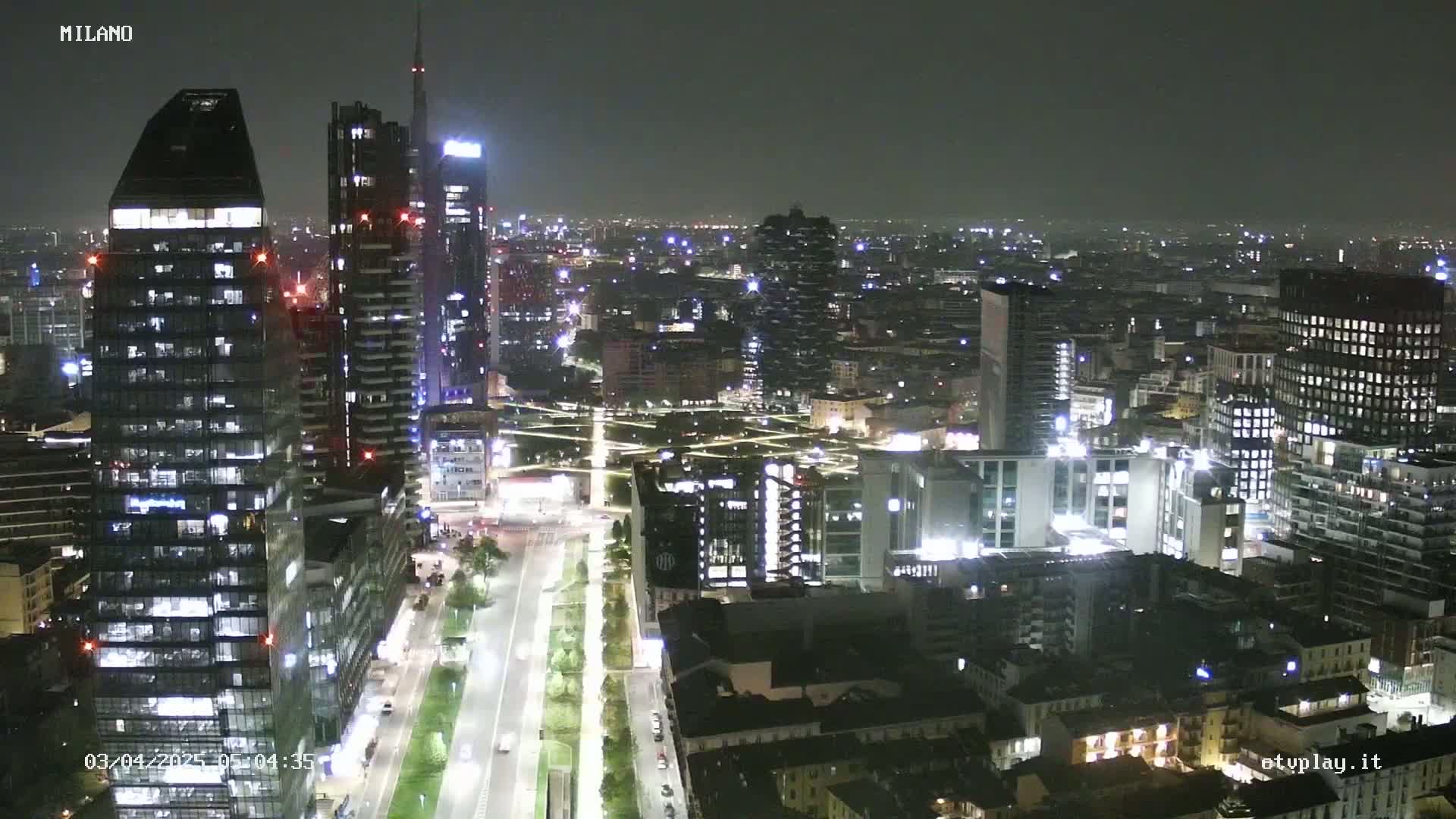 A nighttime aerial view of a city, showing illuminated skyscrapers and streets, under a dark sky.