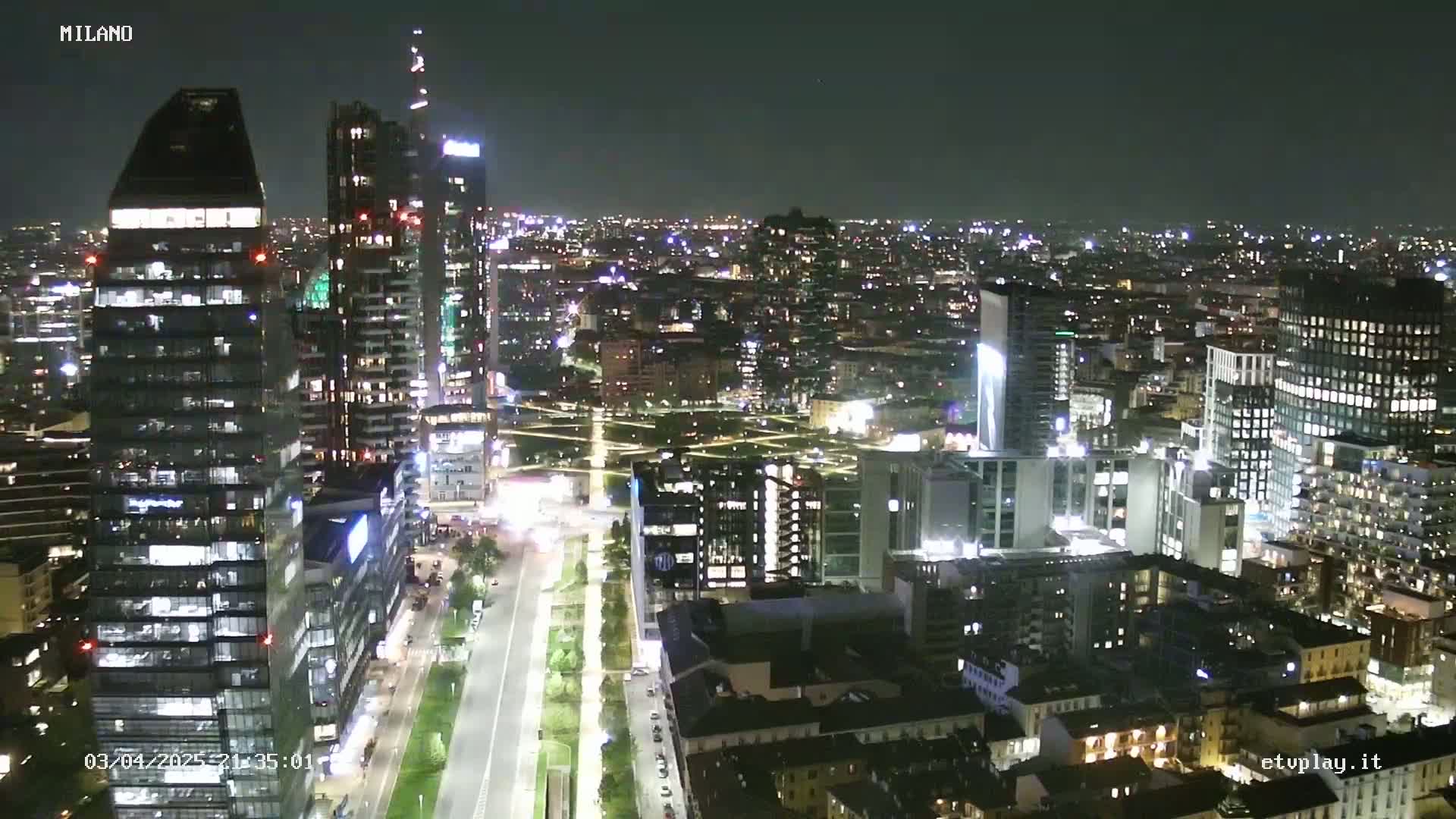 A nighttime aerial view of a city with numerous illuminated skyscrapers and buildings,  under a clear, dark sky.