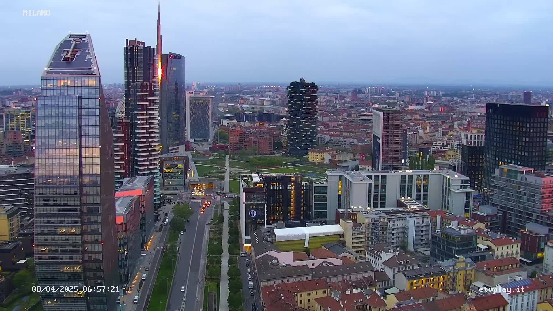 An aerial view of a city skyline at dusk, showing numerous modern skyscrapers and surrounding buildings under a clear sky.