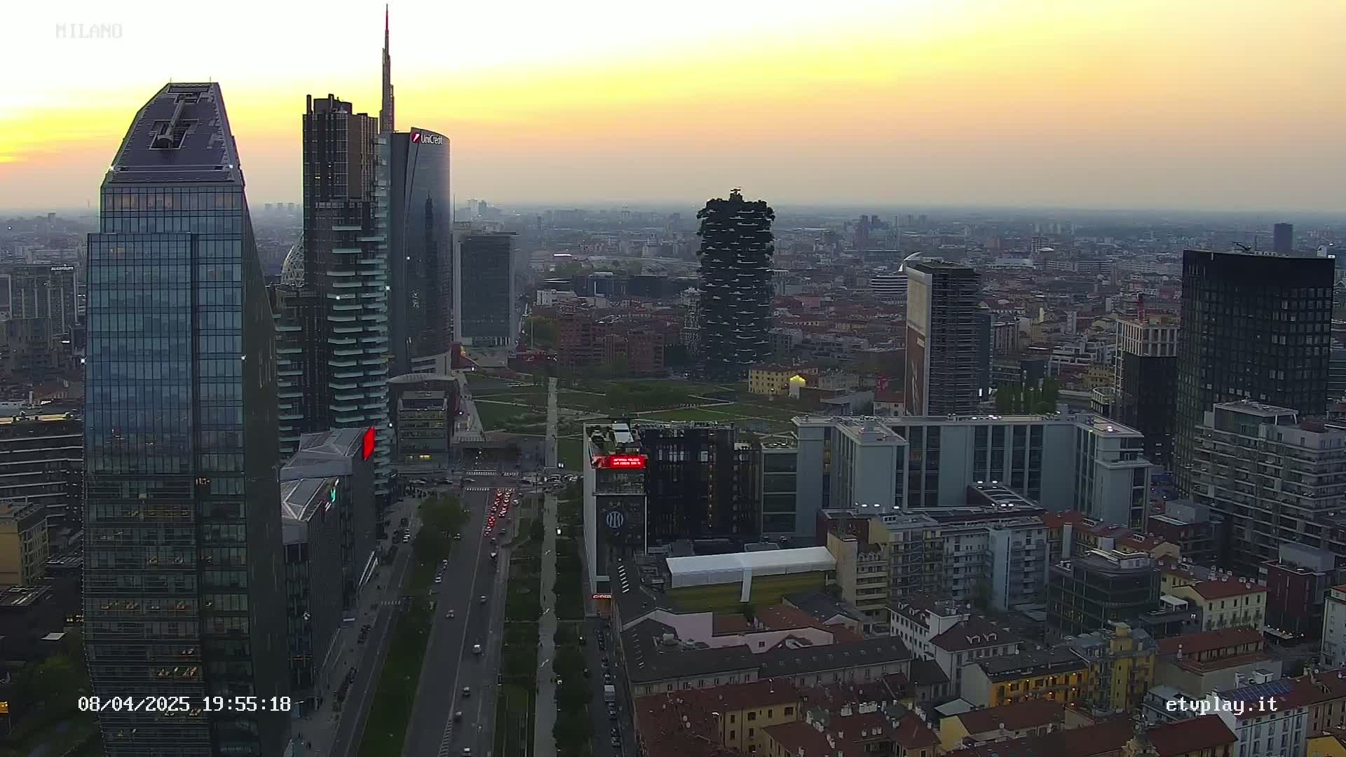 An aerial view of a city skyline at sunset, showing numerous skyscrapers and surrounding buildings.