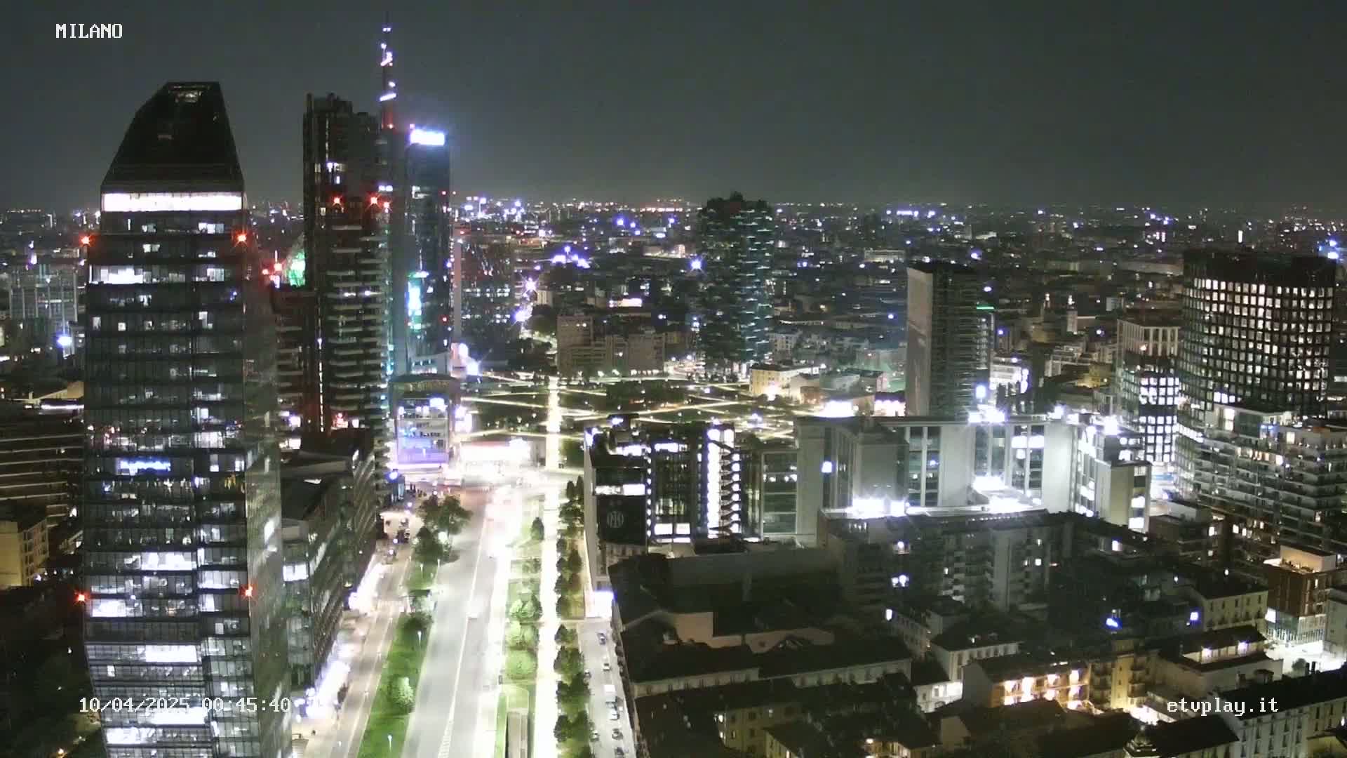 A nighttime aerial view of a city, showing illuminated skyscrapers and streets.
