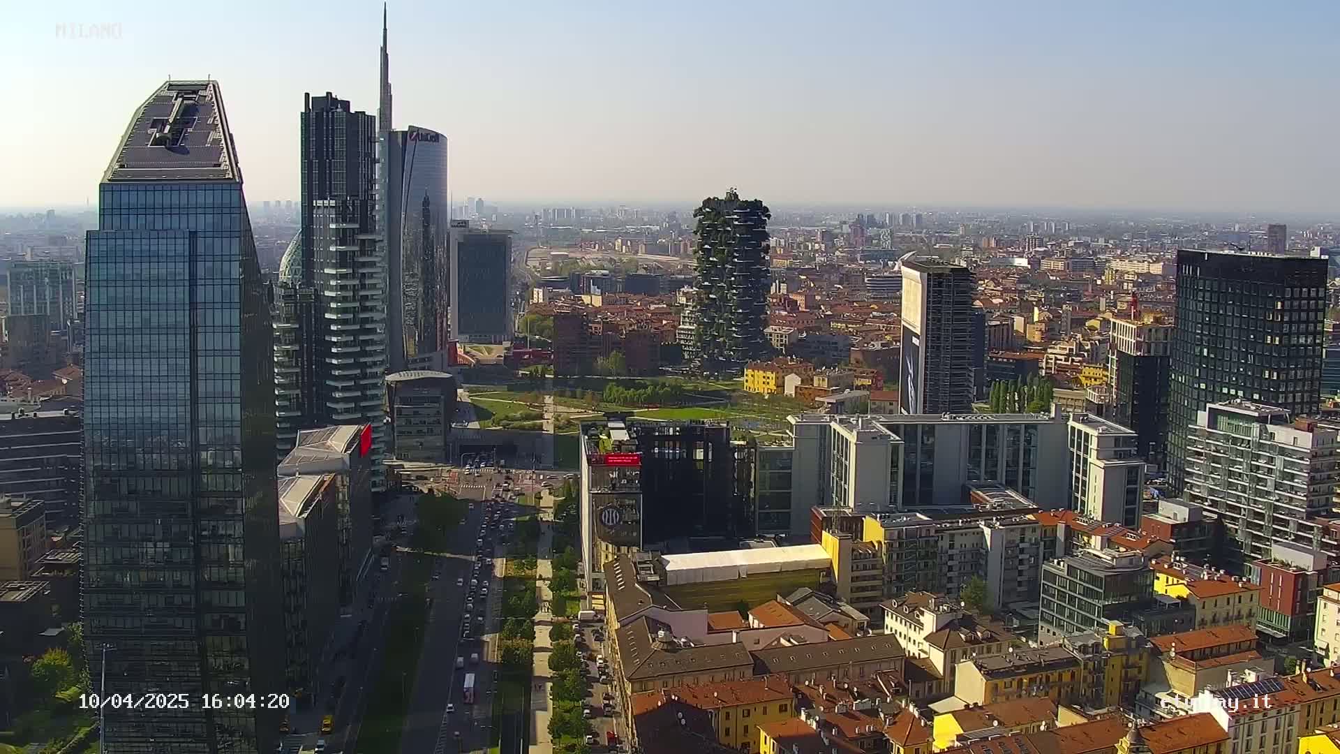 An aerial view of a city skyline on a clear, sunny day, showing a mix of modern skyscrapers and traditional low-rise buildings.