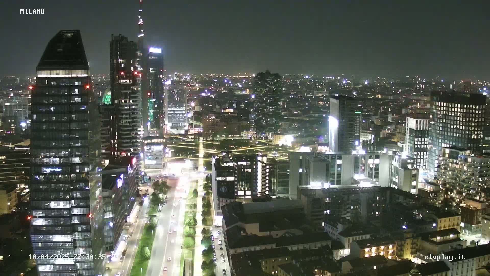 A nighttime aerial view of a city with numerous illuminated skyscrapers and streets, under a clear, dark sky.