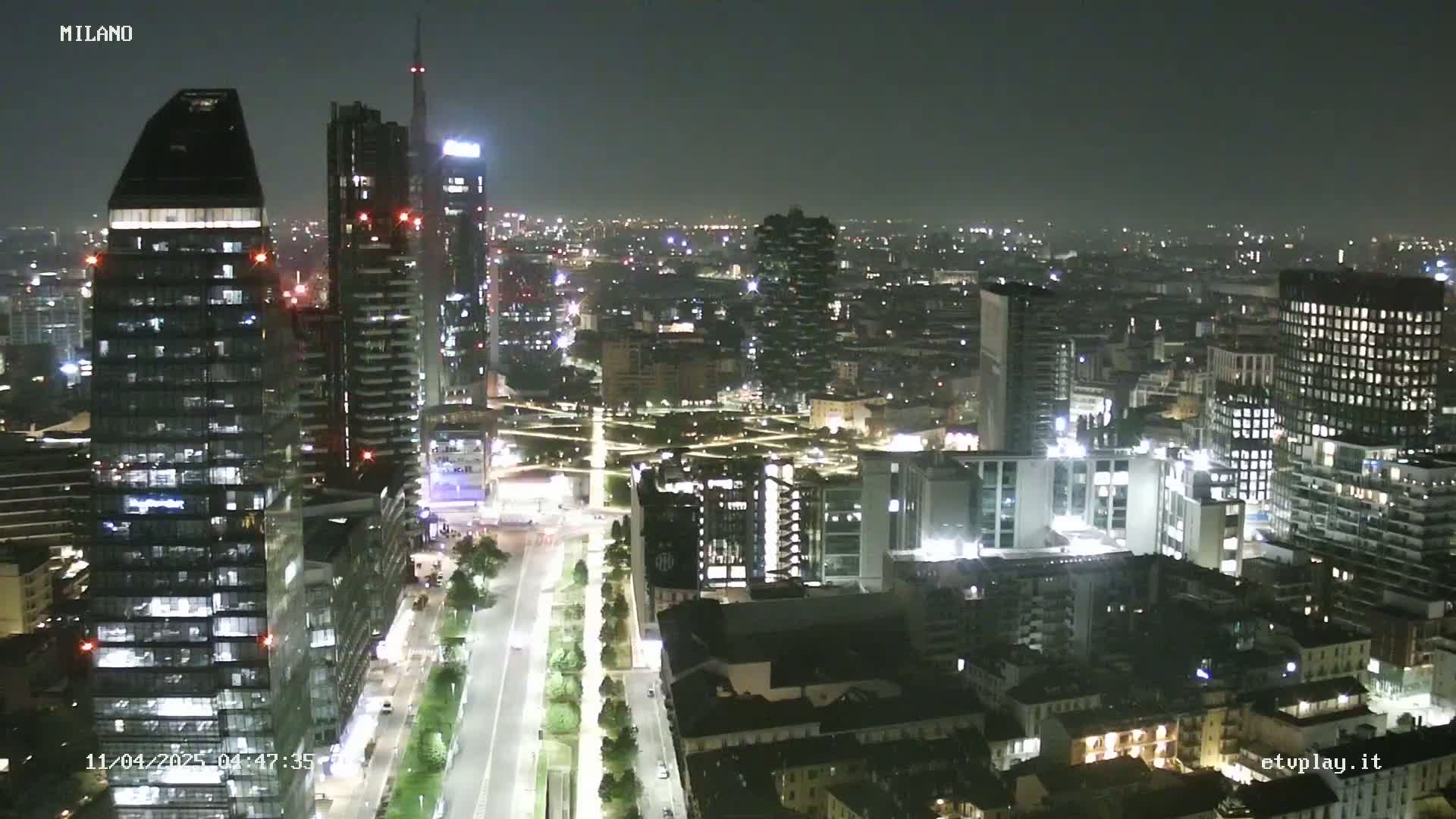 A nighttime aerial view of a city with numerous illuminated skyscrapers and buildings, under a clear, dark sky.