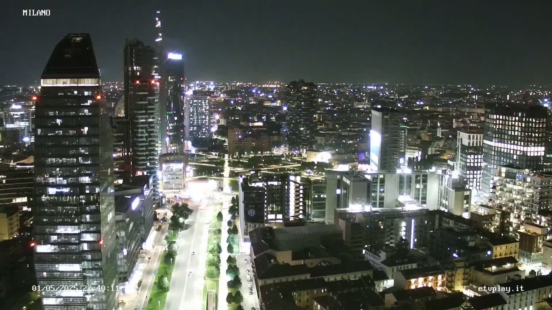A nighttime aerial view of a city with numerous illuminated skyscrapers and buildings, showing a clear sky.