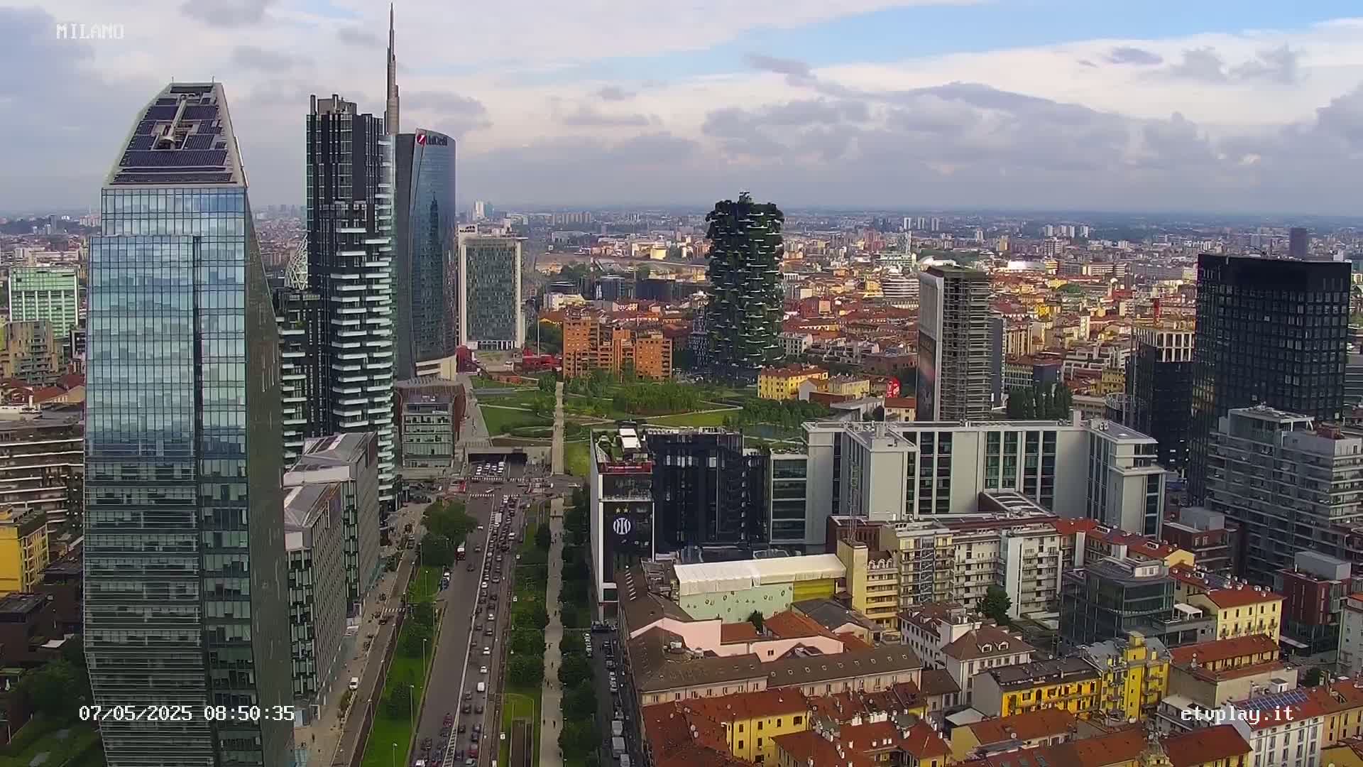 An aerial view of a city with numerous skyscrapers and high-rise buildings under a partly cloudy sky.