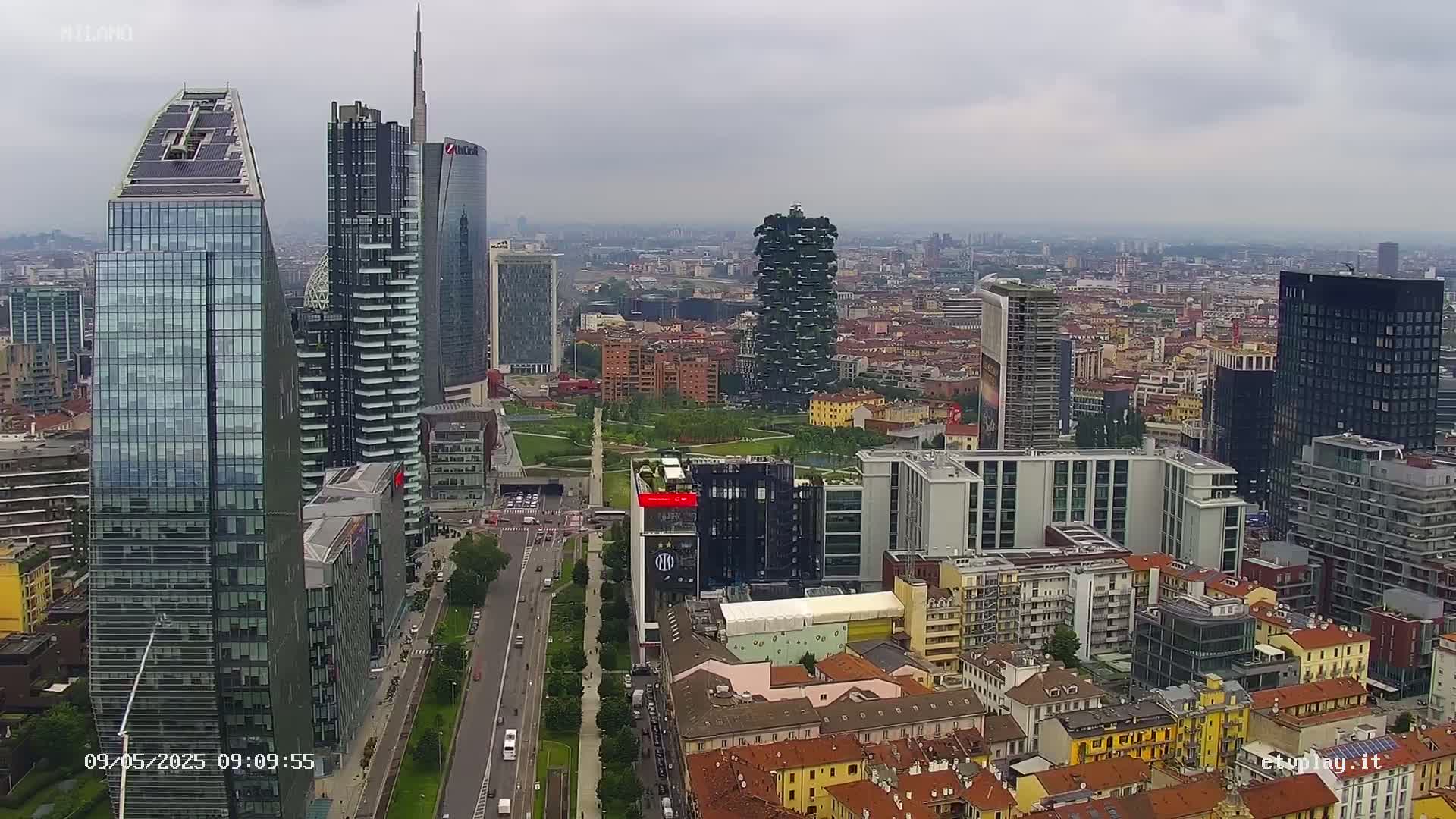 An aerial view shows a city with many skyscrapers under an overcast sky.