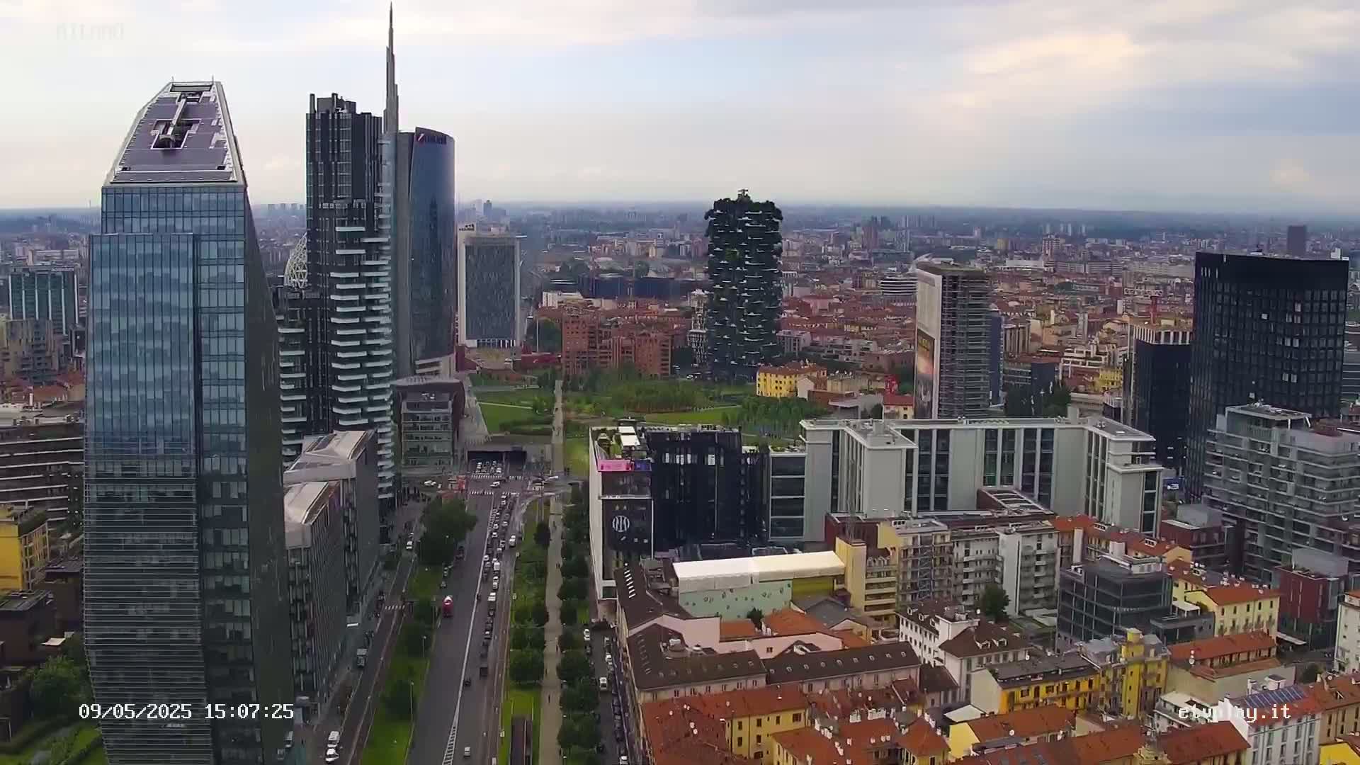 An aerial view of a city with numerous skyscrapers, including a vertical forest, on an overcast day.