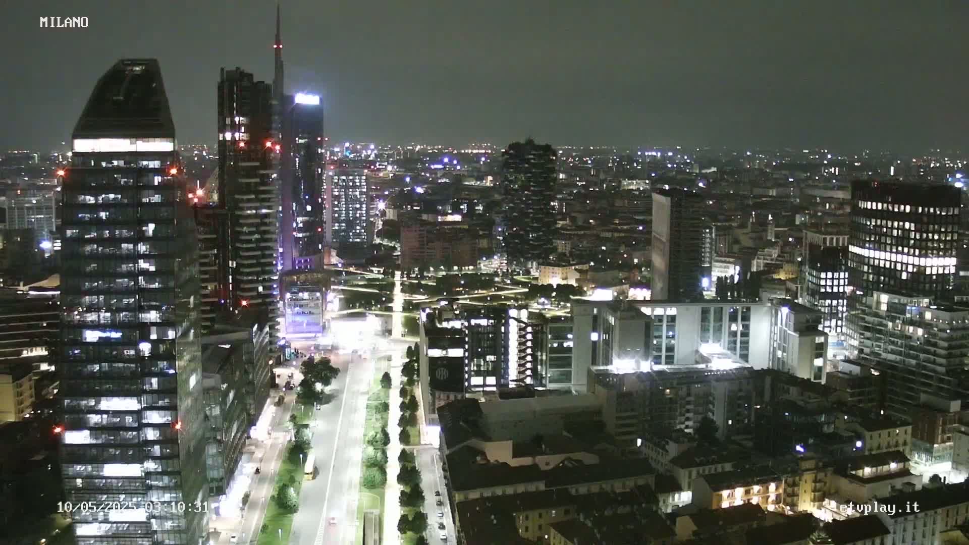 A nighttime aerial view of a city's skyline, showing numerous illuminated buildings and streets.