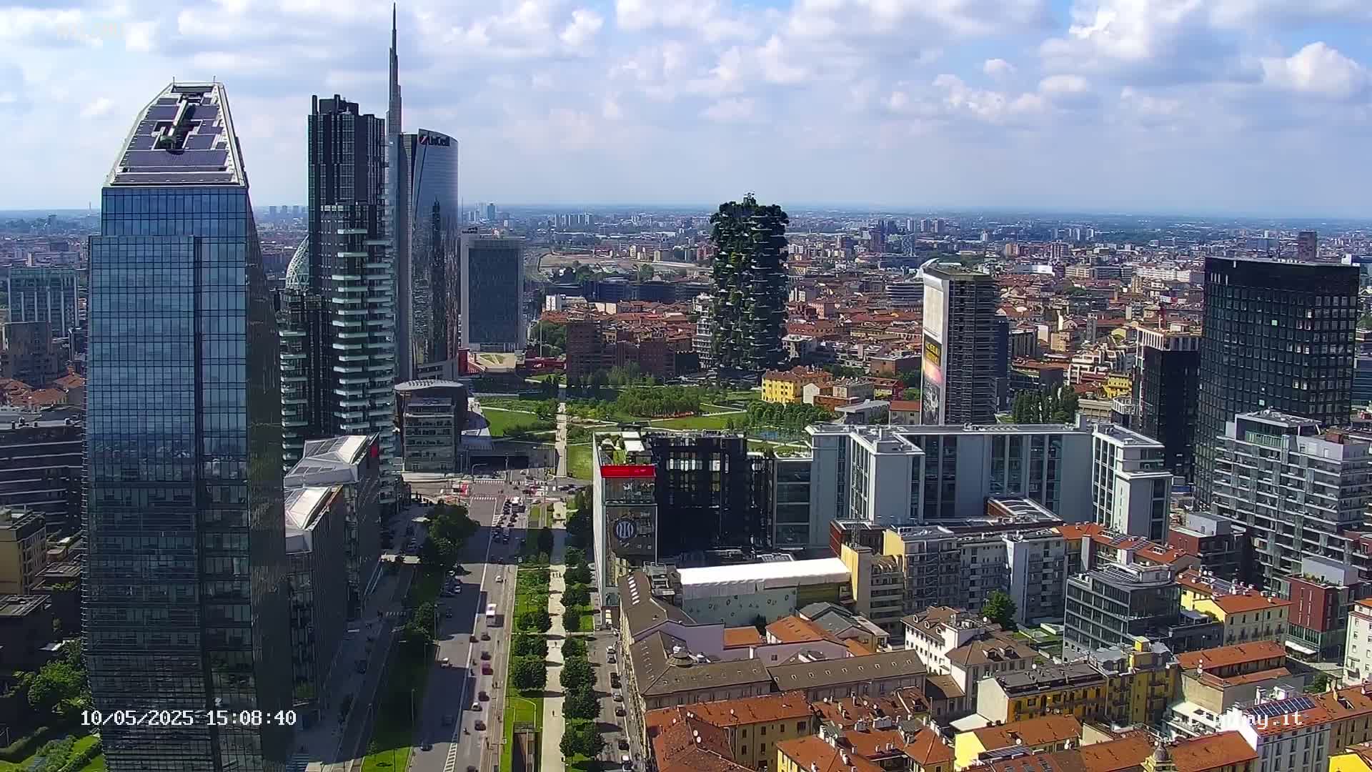 A high-angle, sunny-day view of a city's skyline featuring several modern skyscrapers and a large park, surrounded by lower buildings with red tile roofs.