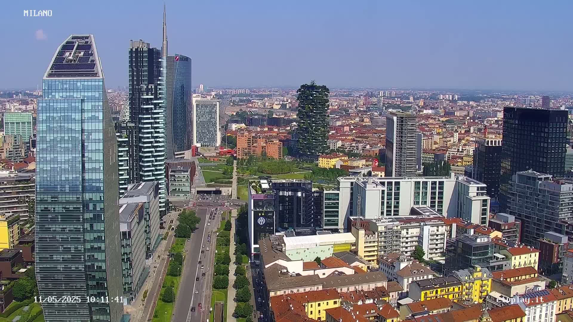 A high-angle, sunny-day view of a city with numerous skyscrapers and surrounding buildings.