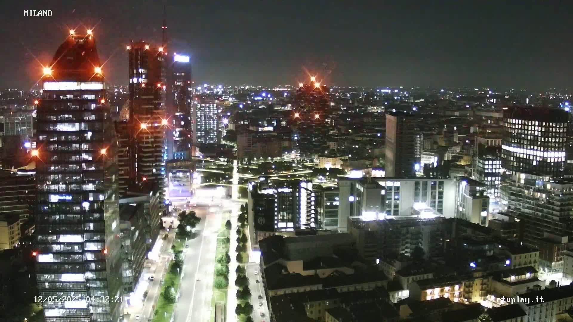 A nighttime aerial view of a city, showing illuminated skyscrapers and streets, under a clear sky.