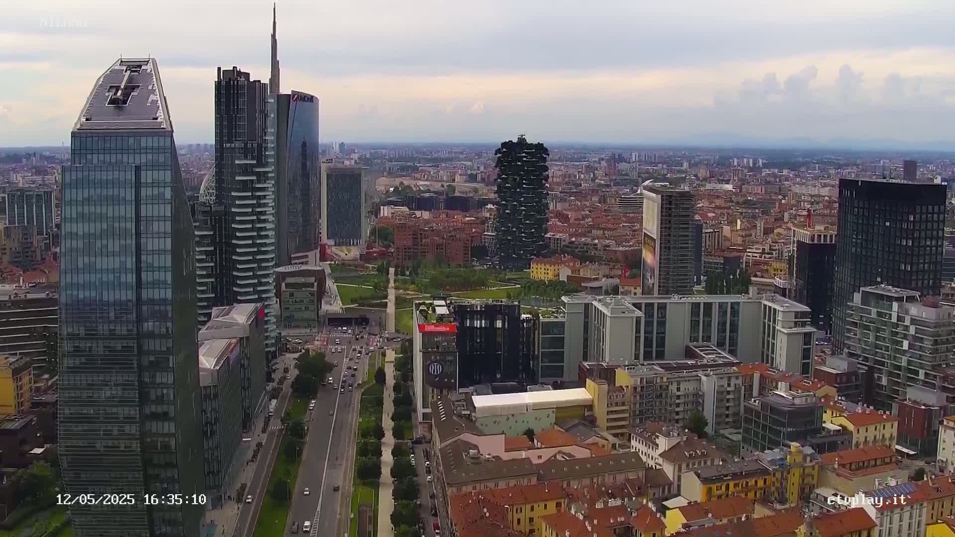 An aerial view of a city's skyline on an overcast day, showcasing numerous modern skyscrapers and a mix of older buildings, with a large park visible in the mid-ground.