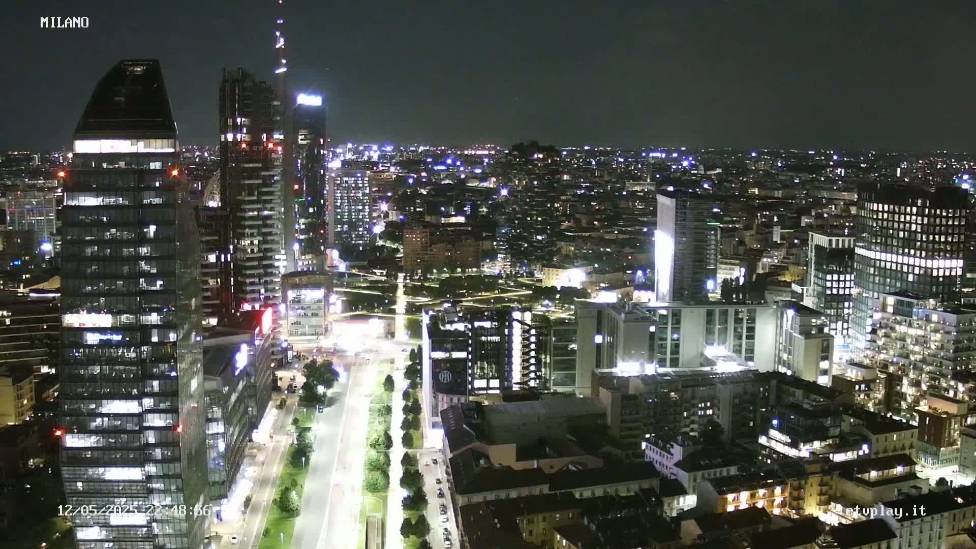 A nighttime, high-angle view of a city skyline with numerous illuminated skyscrapers and buildings extending into the distance under a clear, dark sky.