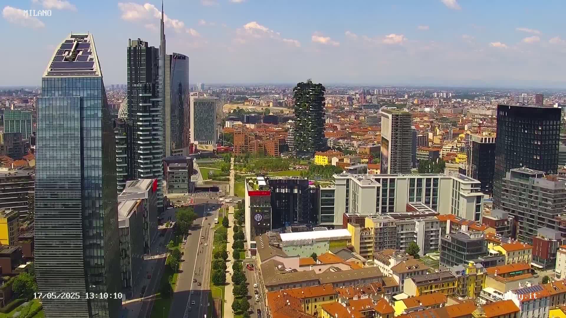 A high-angle, sunny view of a dense cityscape featuring modern skyscrapers and surrounding lower buildings.
