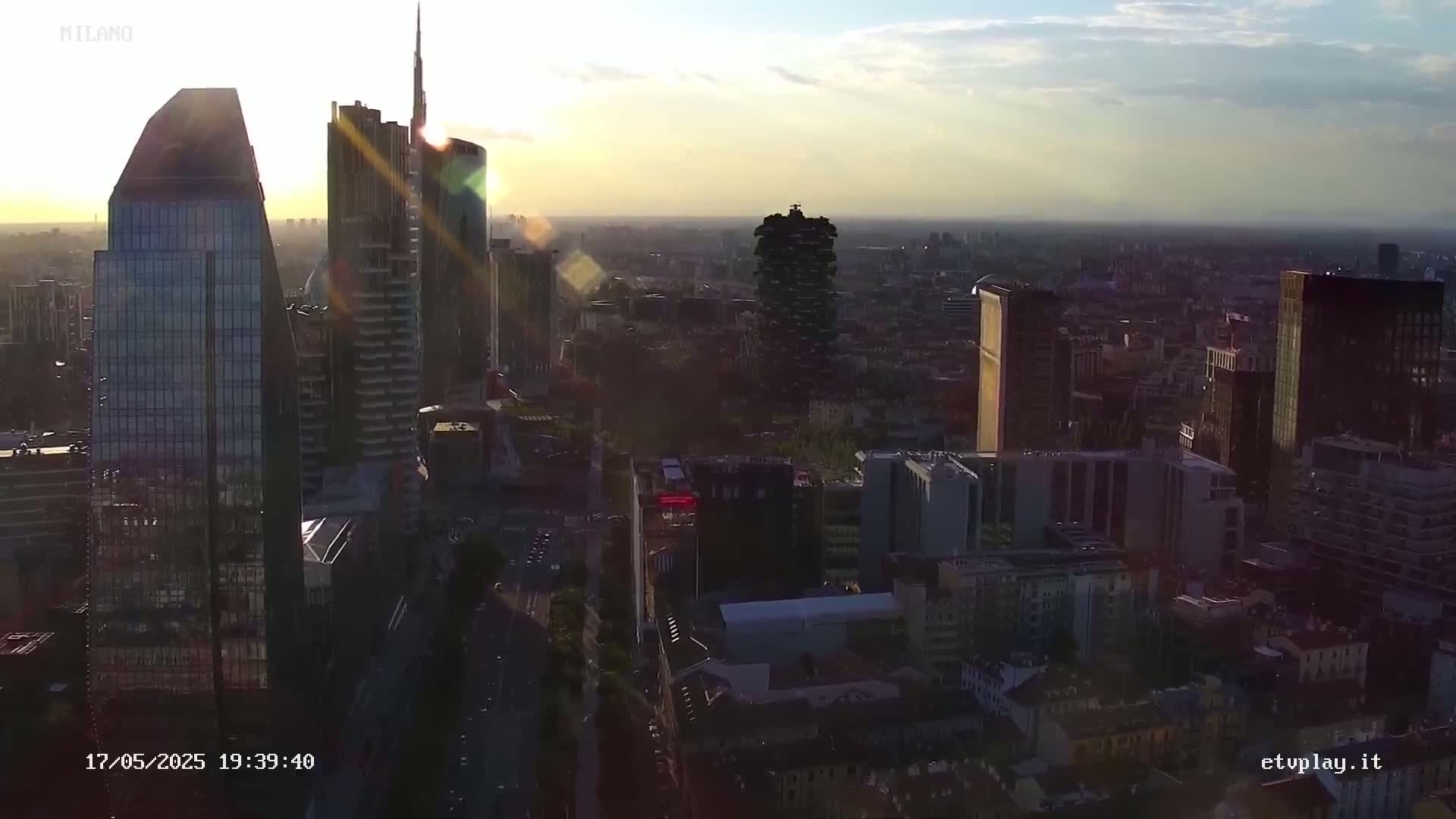 An aerial view of a dense cityscape at sunset, with tall skyscrapers illuminated by the setting sun.