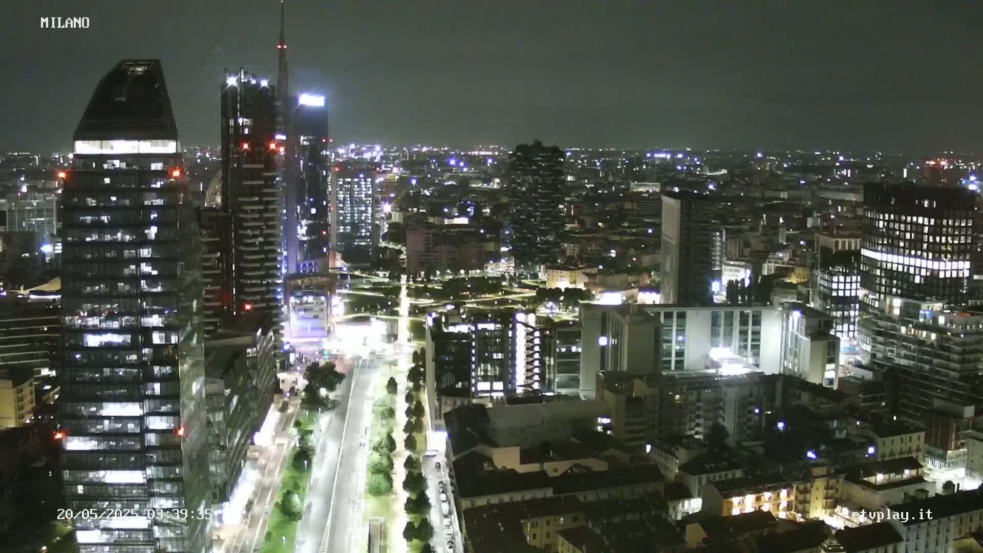 A nighttime aerial view of a city skyline with many tall buildings and brightly lit streets.