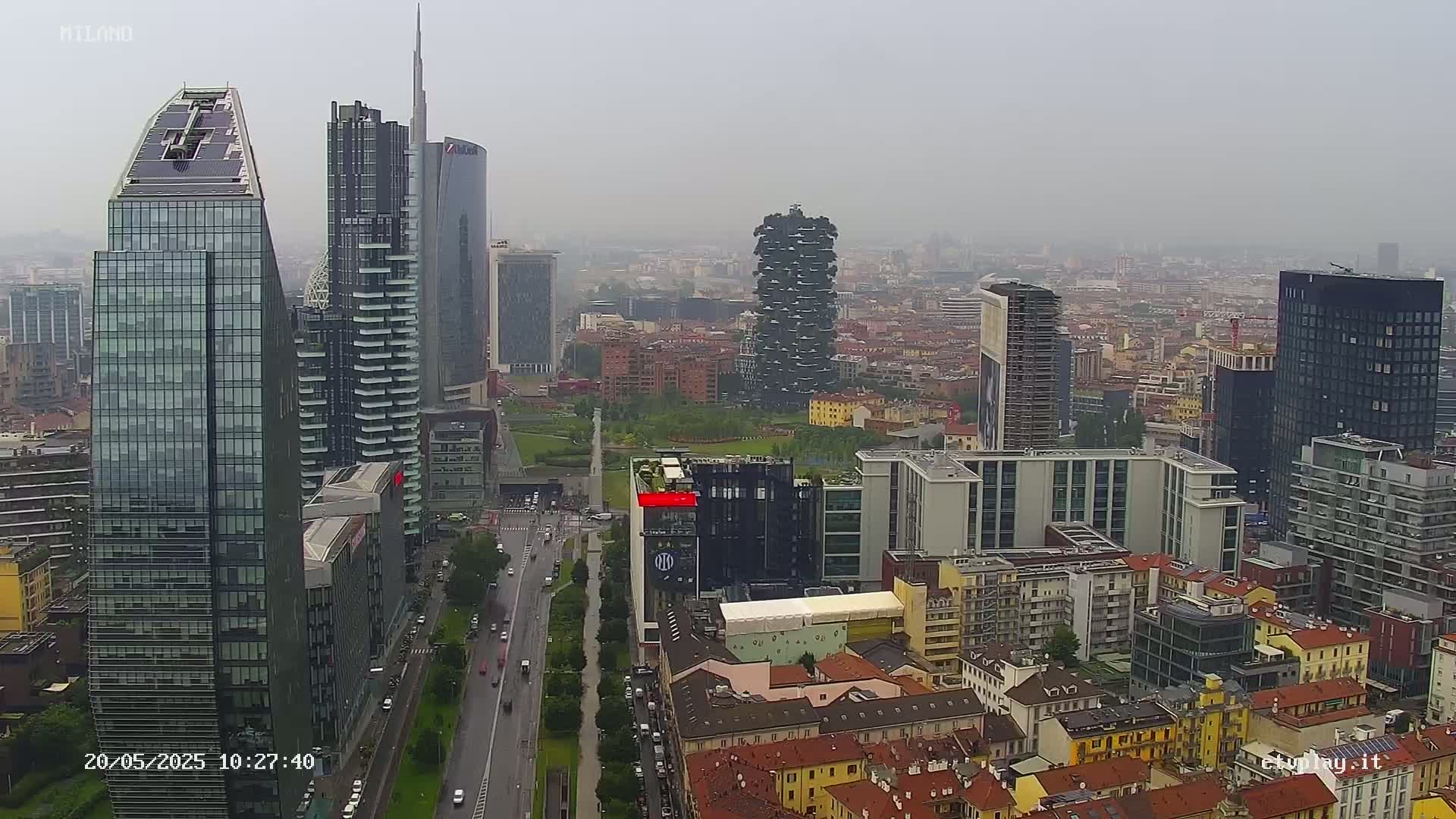 A hazy, overcast day reveals a cityscape of modern and older buildings, with several skyscrapers prominent in the foreground, and a vast expanse of city stretching into the distance.