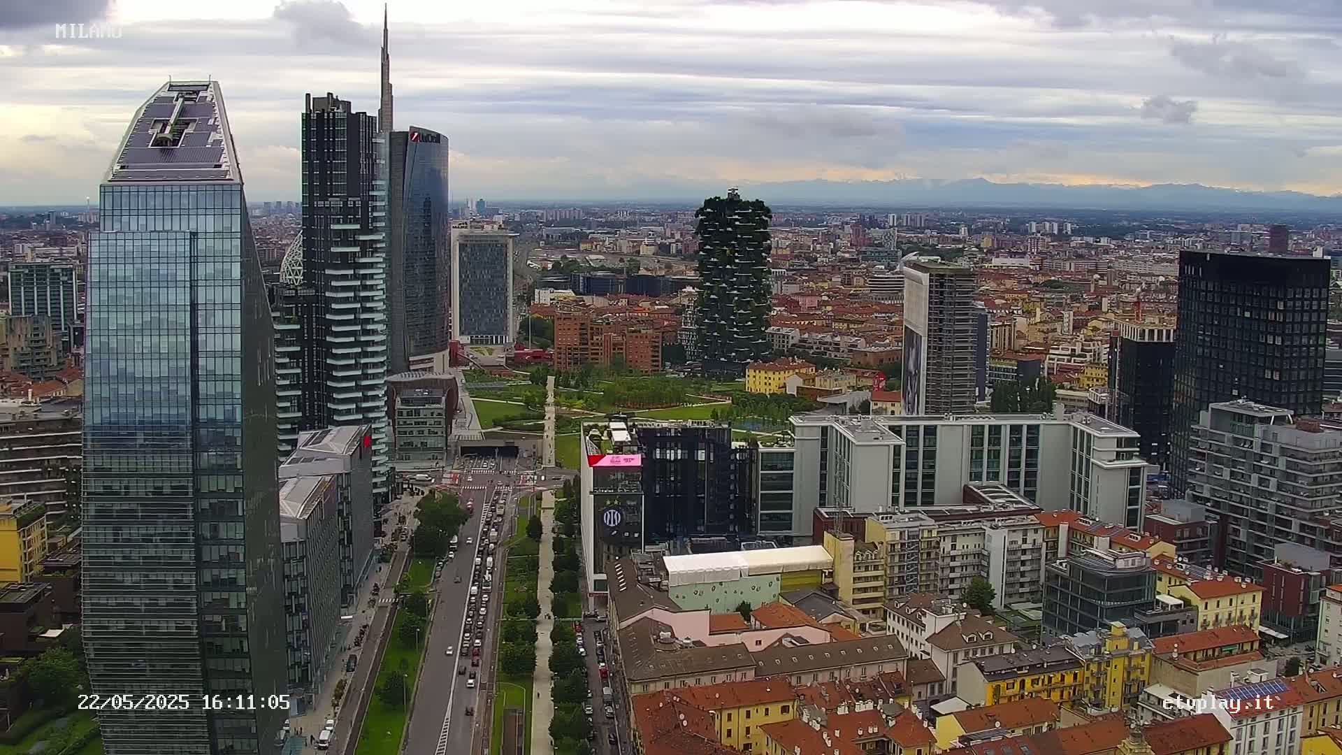 An aerial view of a city skyline with modern skyscrapers and a partly cloudy sky shows a city under overcast conditions.