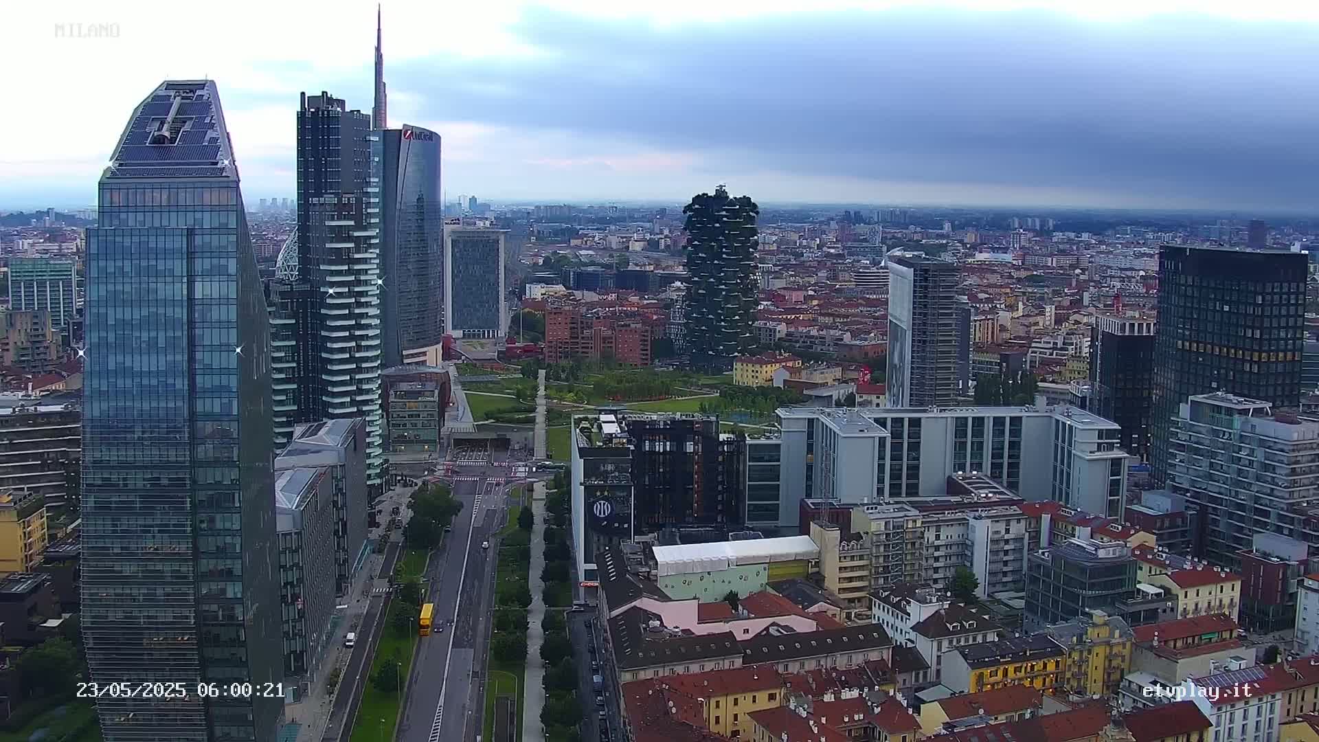 An aerial view of a city's skyline on an overcast day, showing a mix of modern skyscrapers and older buildings, with a large park visible in the midground.