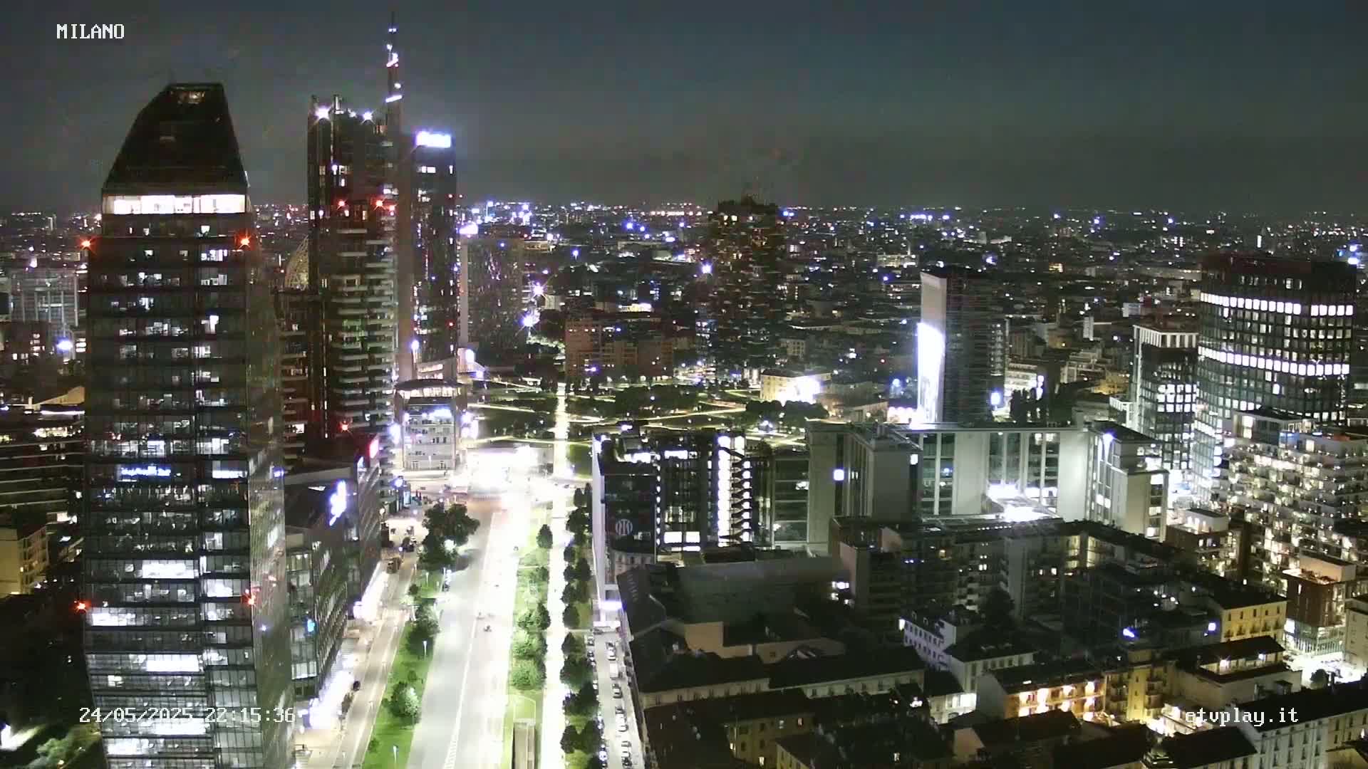 A nighttime aerial view of a city skyline with numerous illuminated skyscrapers and buildings, showing a clear night sky.