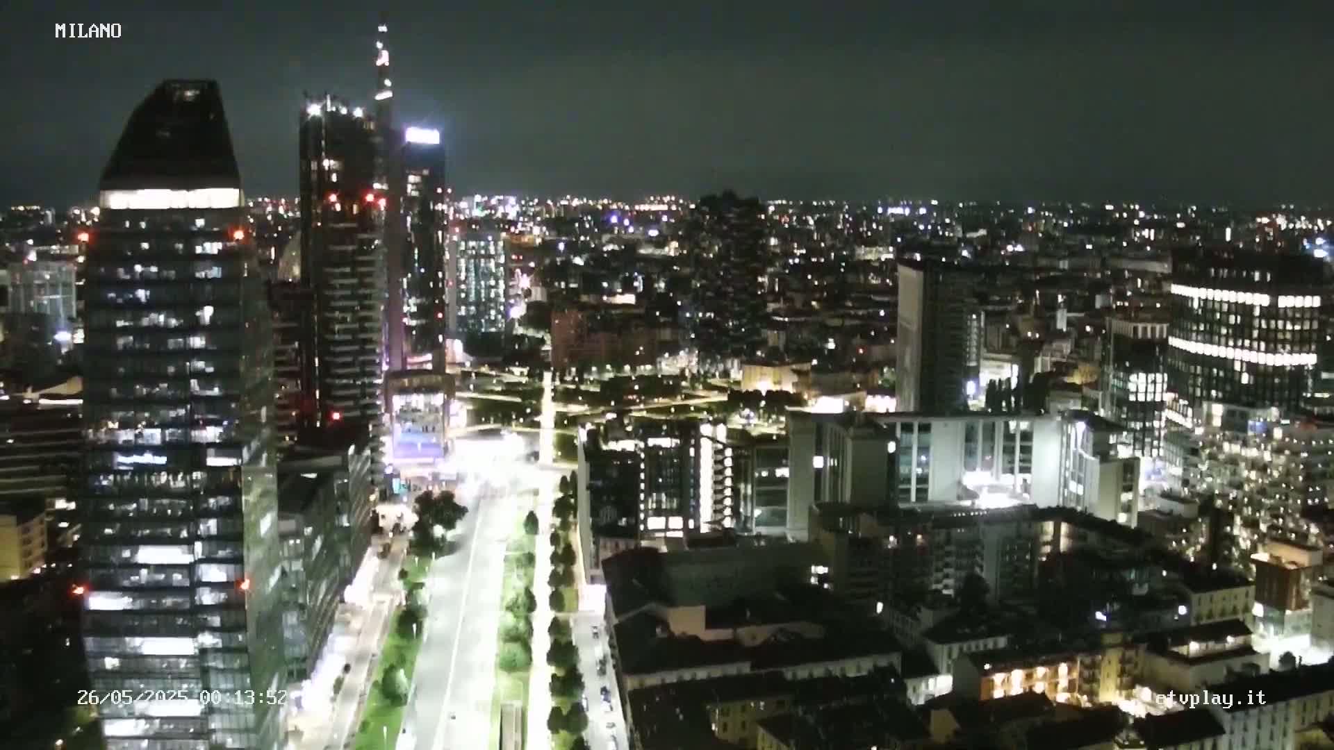 A nighttime aerial view of a city, showing brightly lit skyscrapers and streets, under a clear, dark sky.