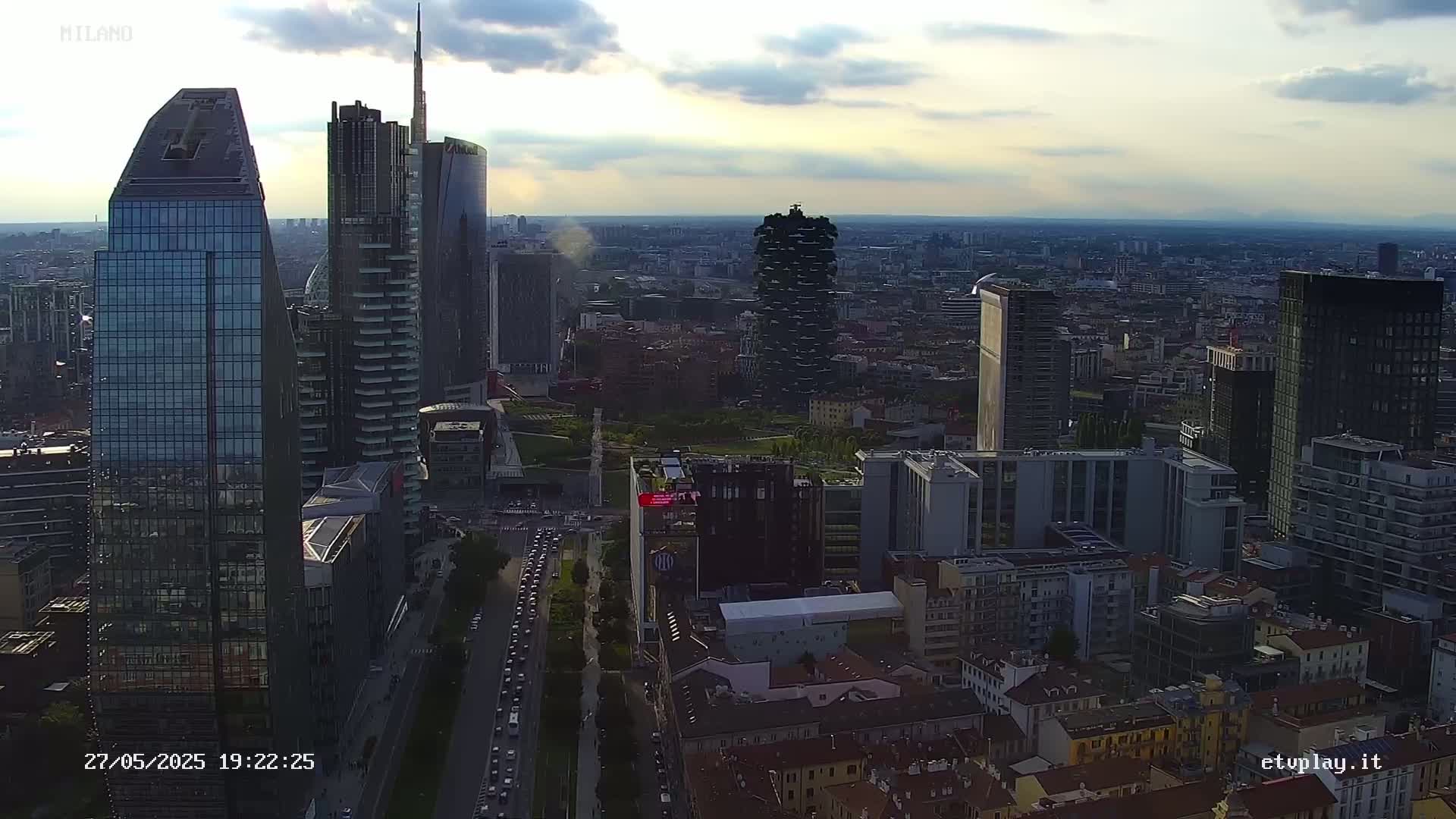 A high-angle, long shot of a city skyline at sunset or dusk, with several skyscrapers visible under partly cloudy skies.